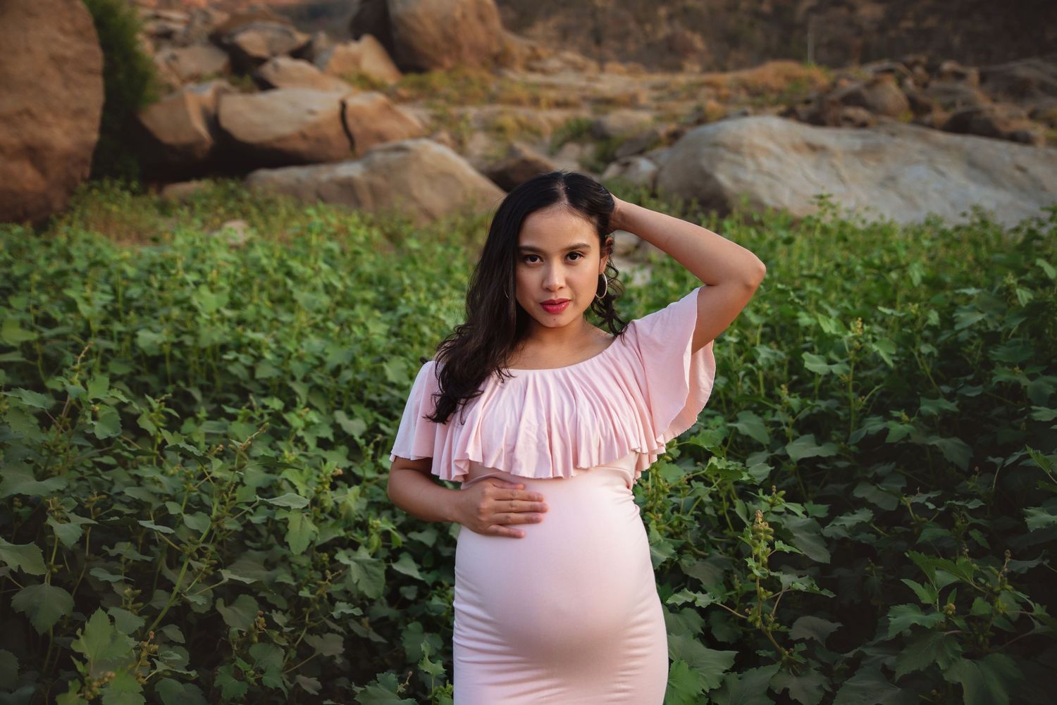 A woman in a pink off-shoulder top poses in a lush garden setting during golden hour, Visalia maternity photography