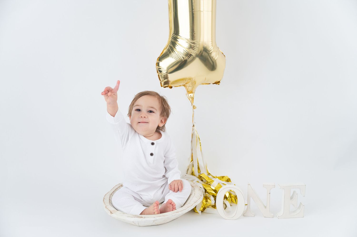 First birthday celebration setup with gold decorations and white backdrop. Hanford Cake Smash Photos