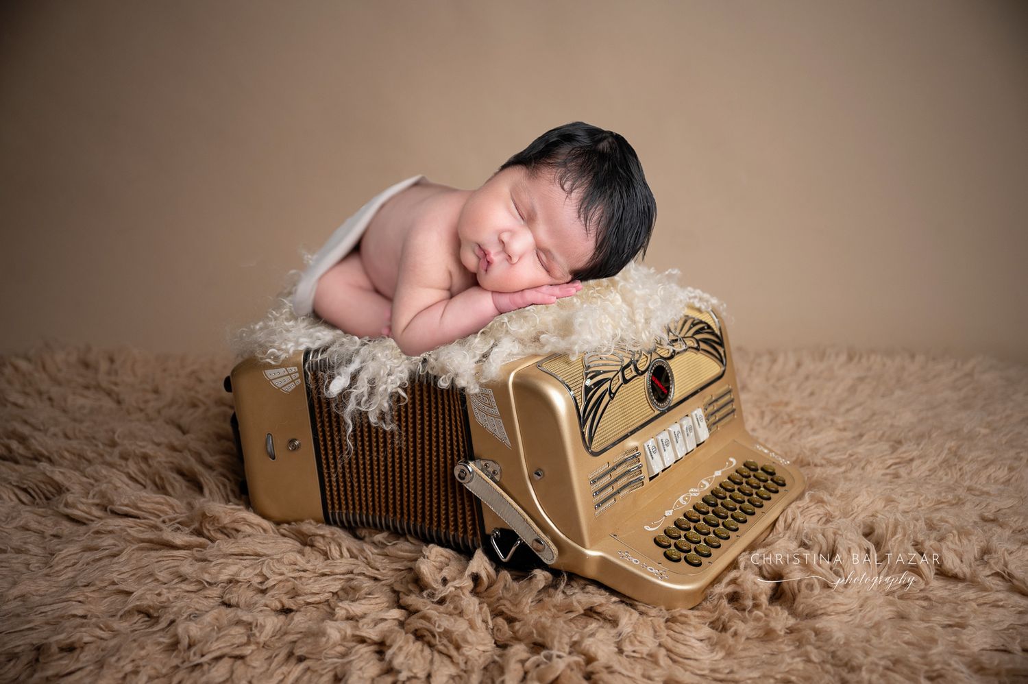 A sleeping newborn baby rests peacefully on an accordion with a beige backdrop. Fresno Newborn Photographer