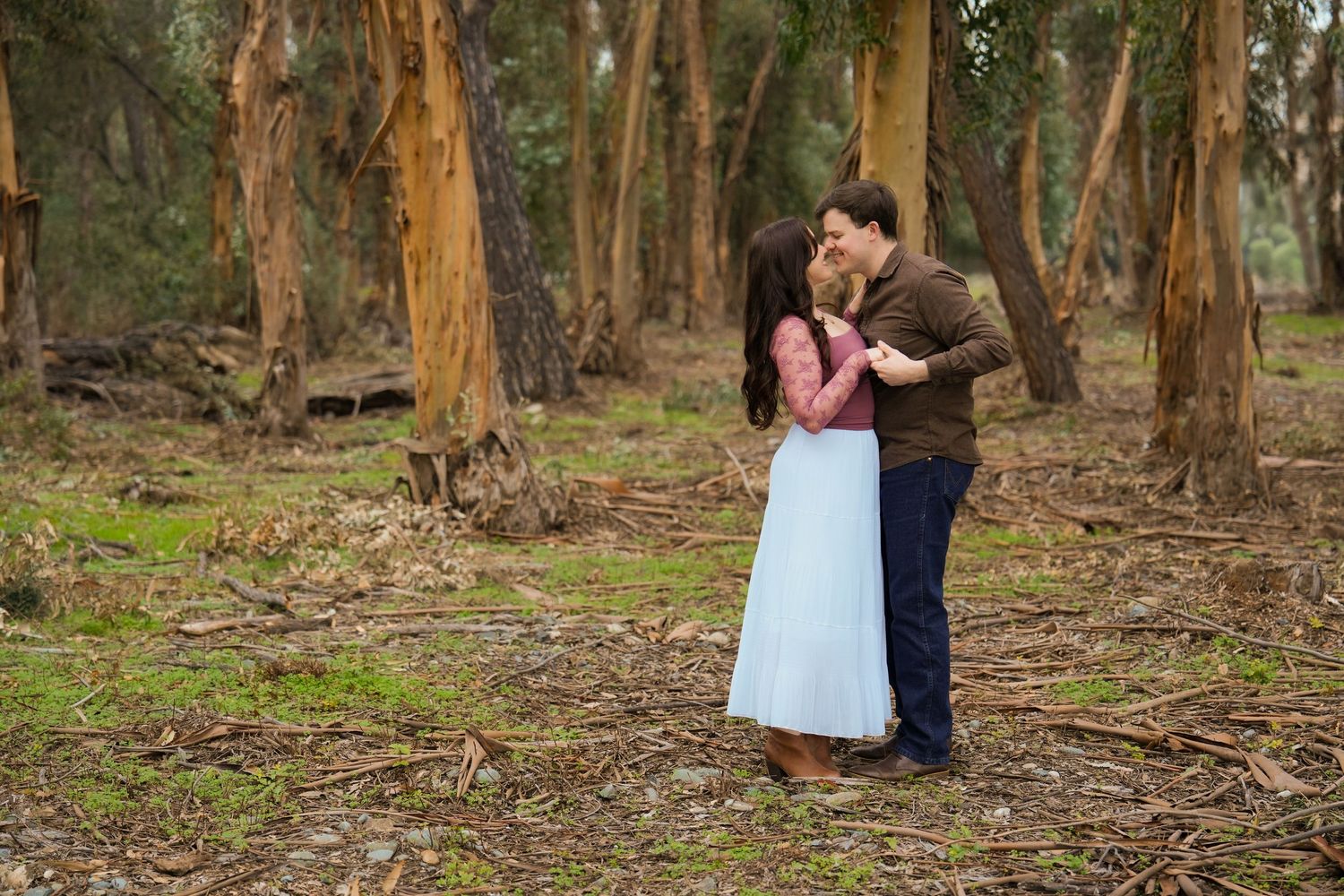 A couple shares a romantic moment while dancing together in a eucalyptus forest.