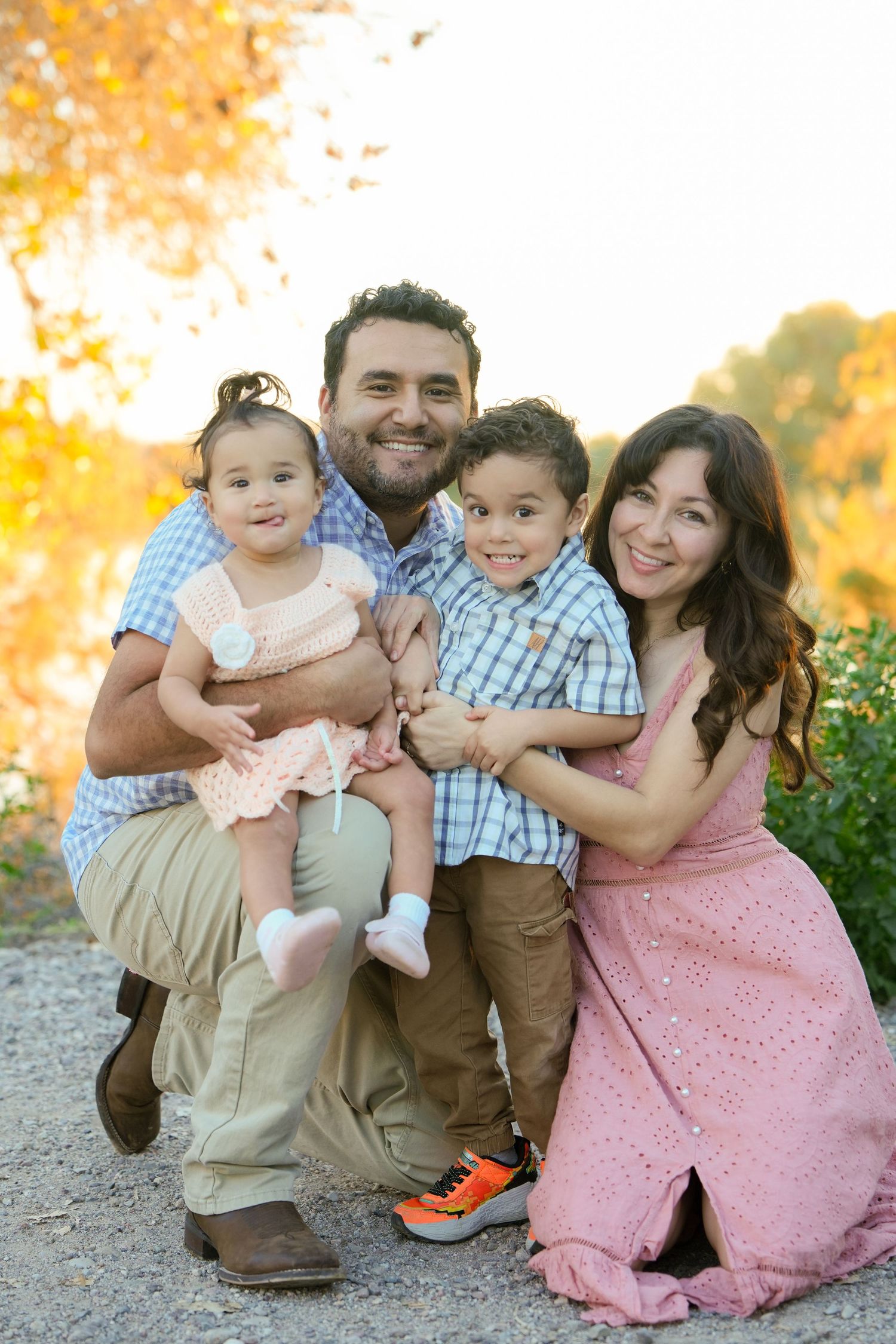 A family wearing coordinated pink and blue outfits poses together outdoors during golden hour in autumn.