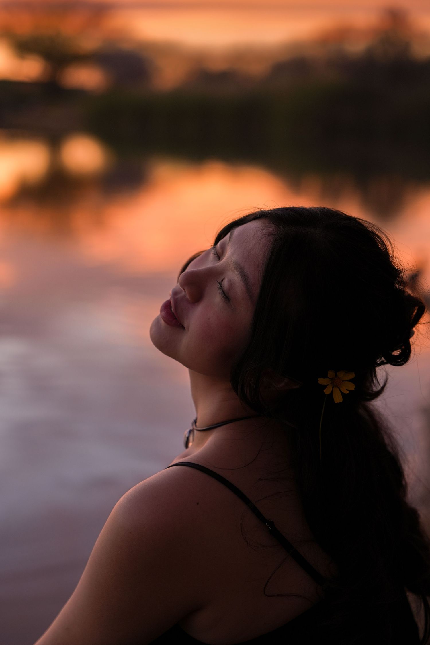 Silhouette of figure in profile against sunset sky over water with warm orange glow.