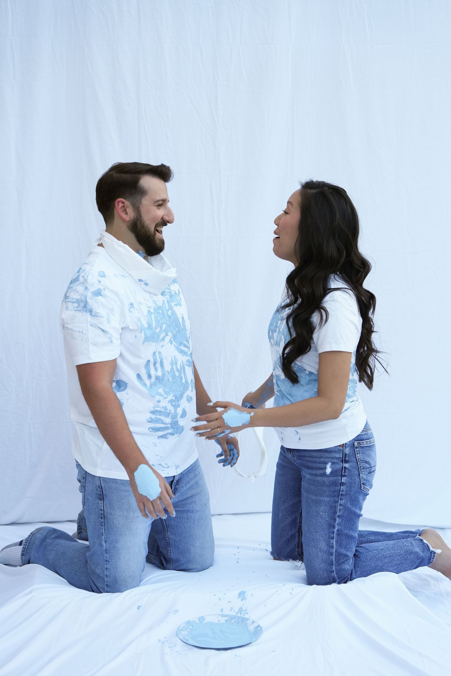 A couple in matching white shirts and jeans sitting together and sharing playful moments on a white background.