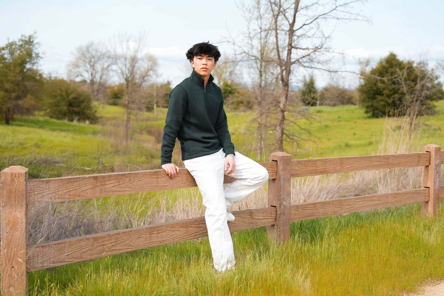 A person in black sits on a wooden fence overlooking a scenic rural landscape.