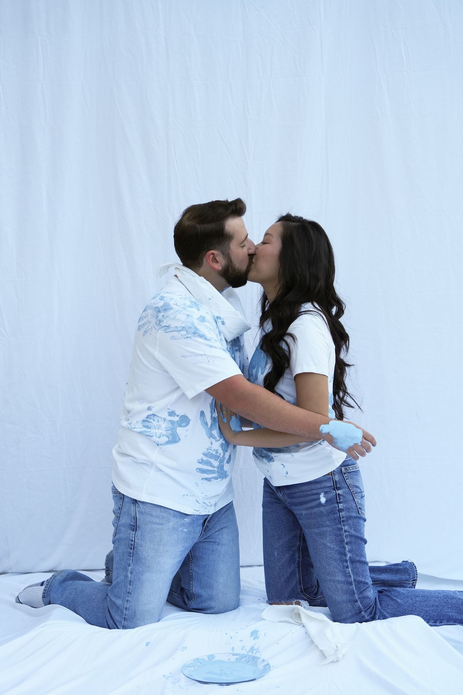 A couple wearing matching denim and white outfits share a romantic moment against a white background.