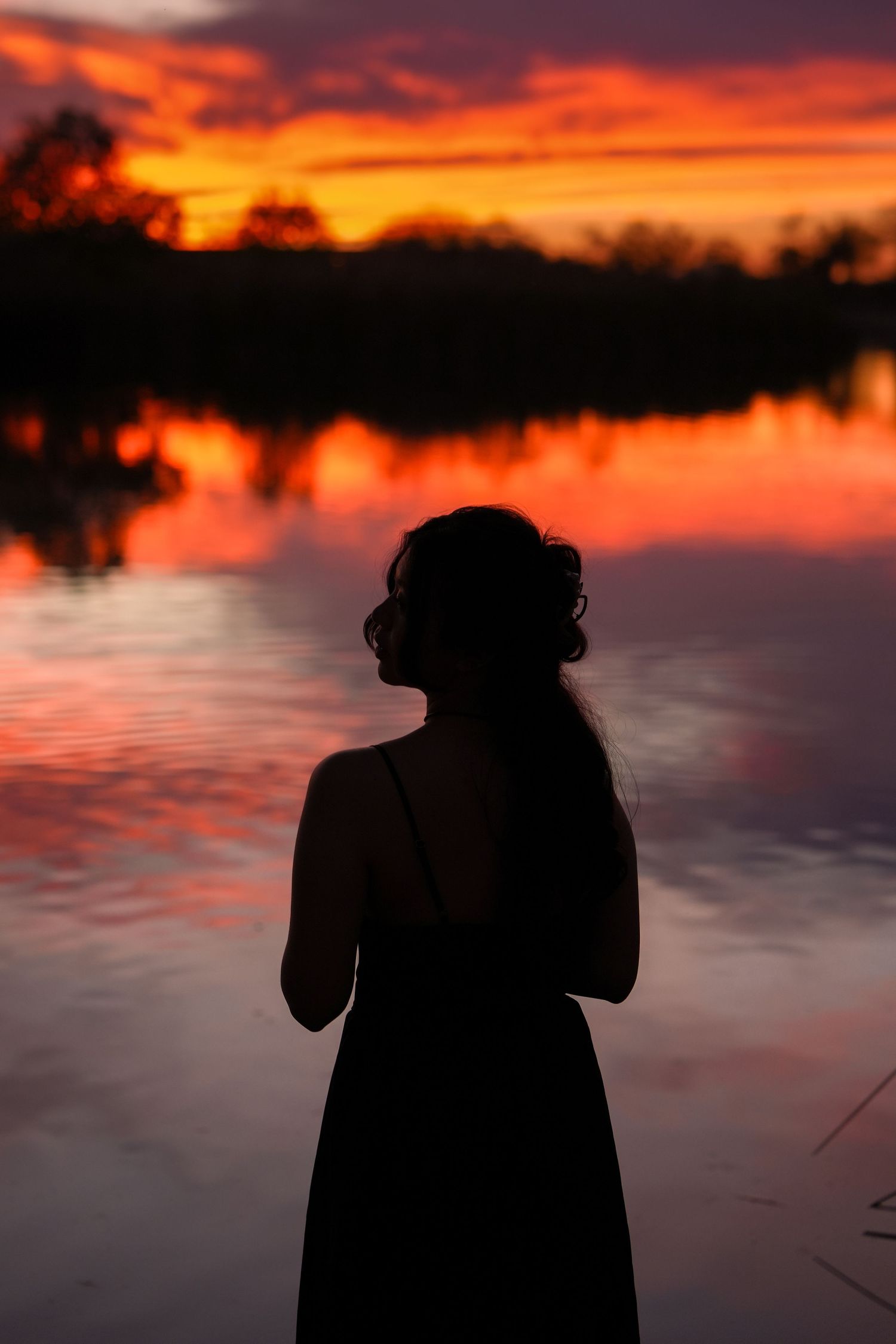 Dark silhouette of a photographer against a dramatic orange sunset reflecting on still water.