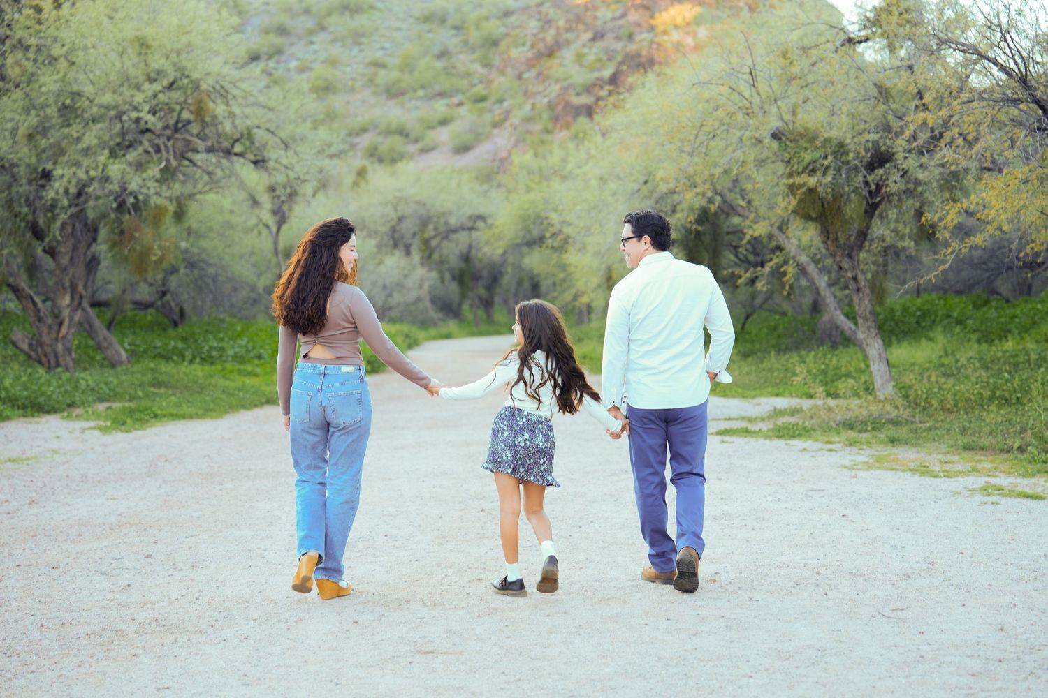 Three people walking together on a winding dirt path through green hills during sunset.