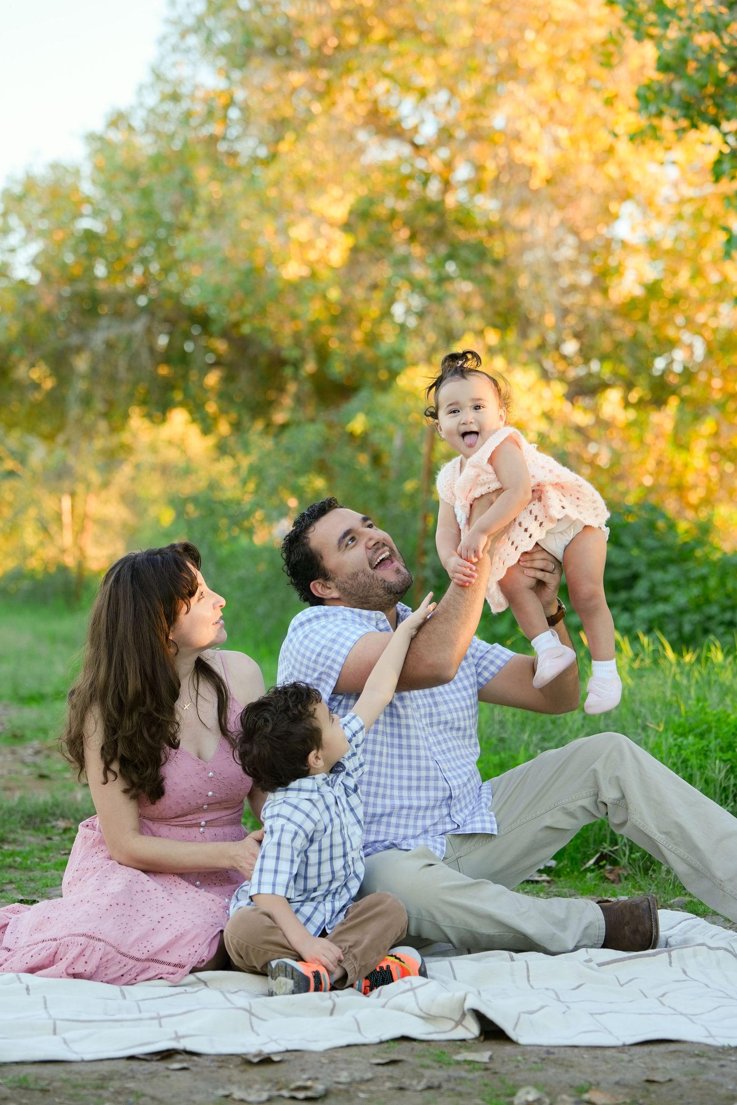 A family enjoys a picnic together on a blanket during golden hour with autumn trees in the background.