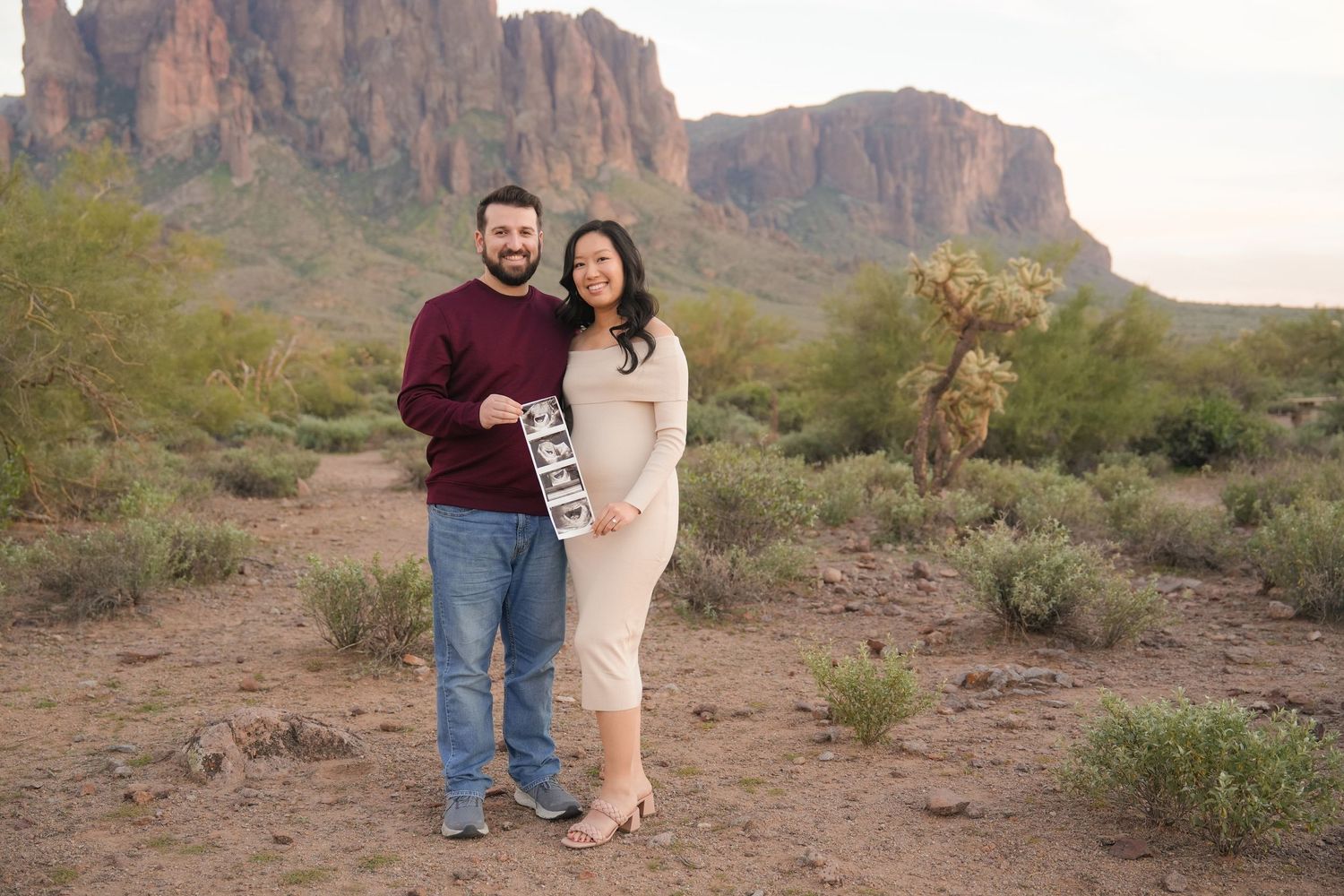 Couple holds ultrasound photo in Arizona desert with Superstition Mountains backdrop during maternity photoshoot.