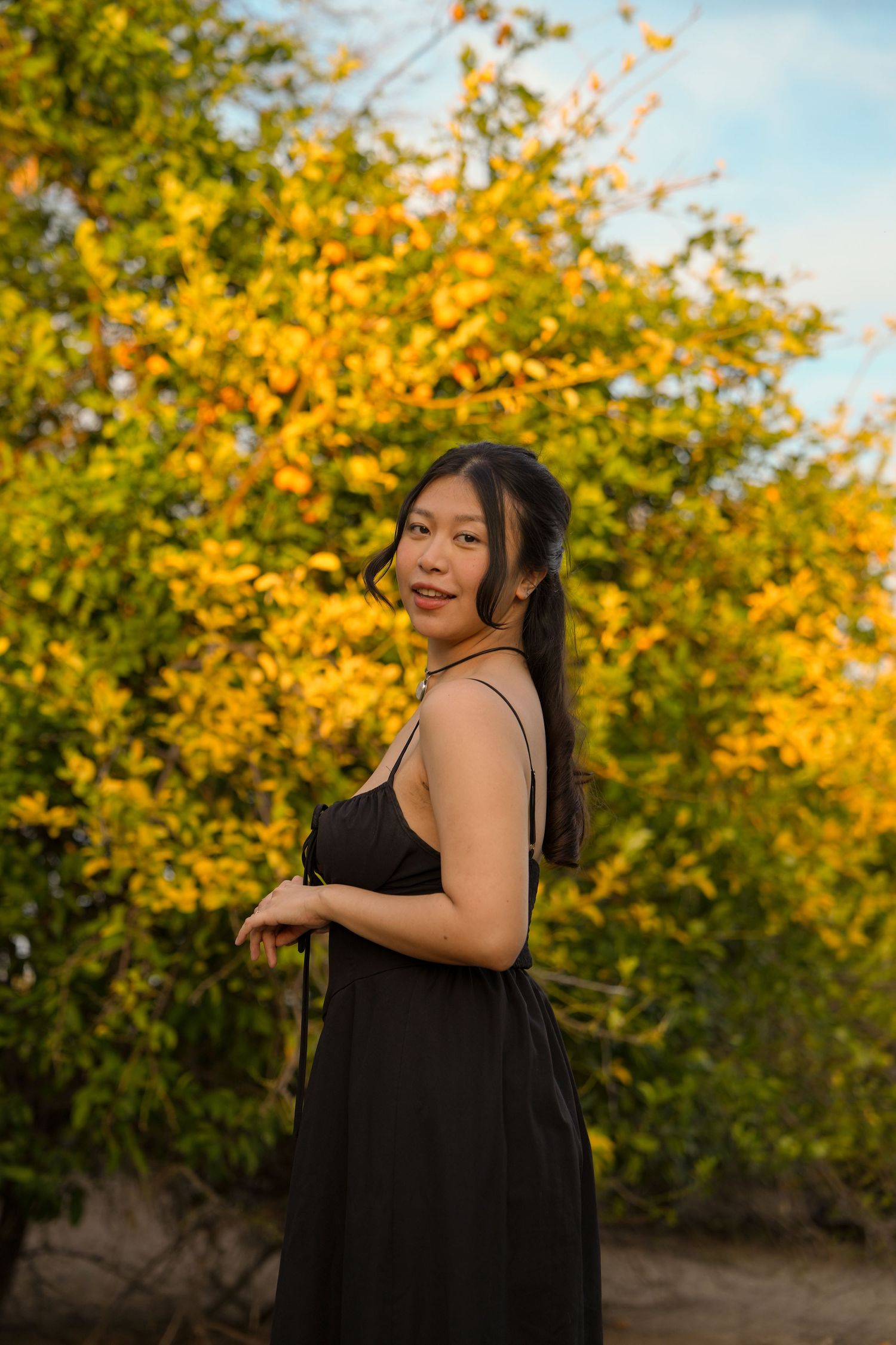 A woman in a black dress poses against vibrant yellow autumn foliage in a series of outdoor portraits.
