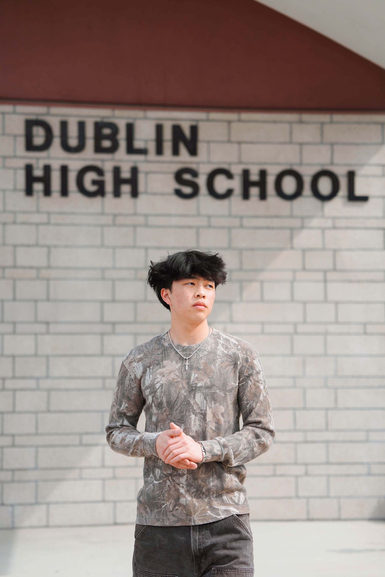 Young man in camo shirt stands confidently in front of Dublin High School brick wall sign.