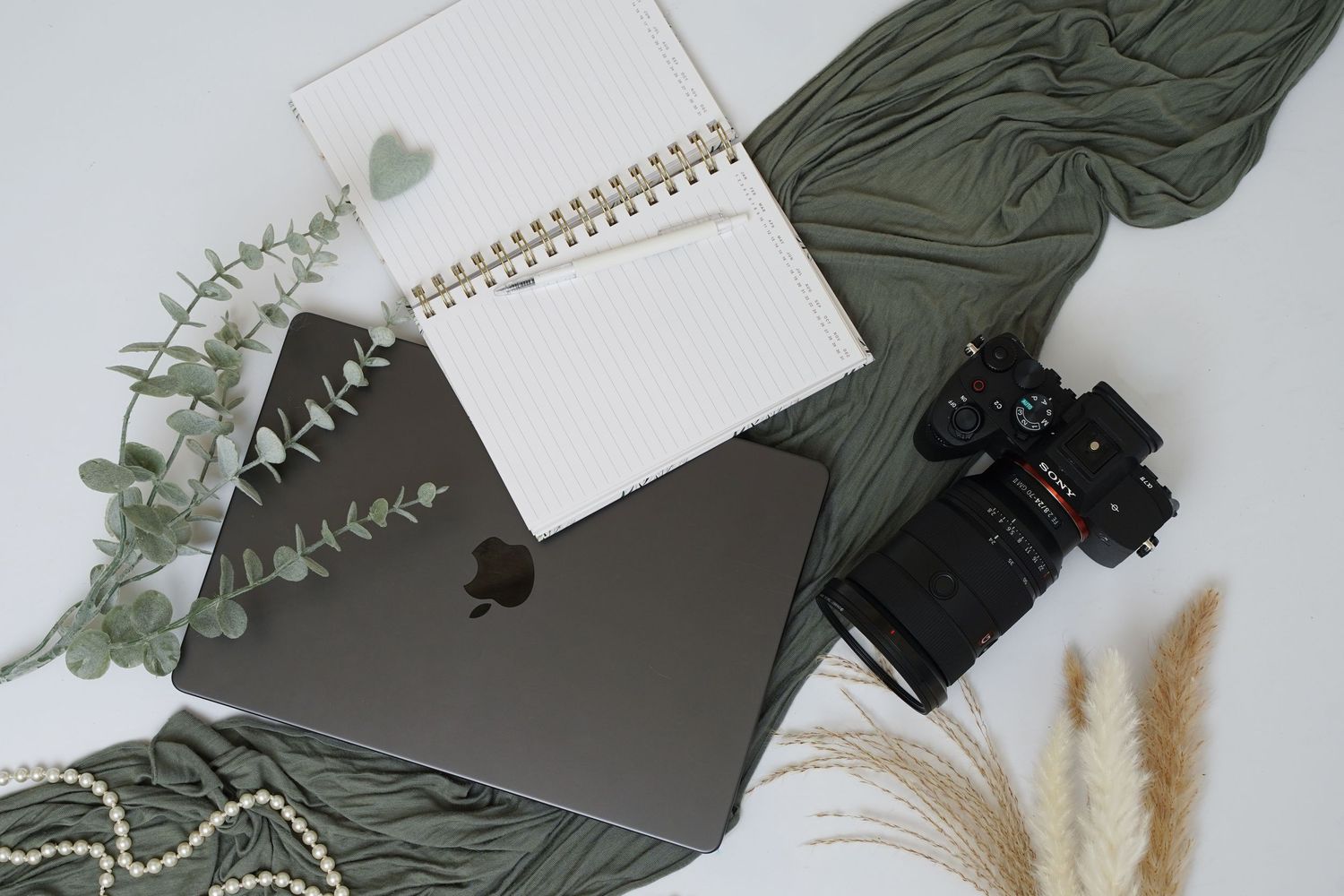 Flat lay of dark green notebook with decorative items and eucalyptus leaves on white surface.