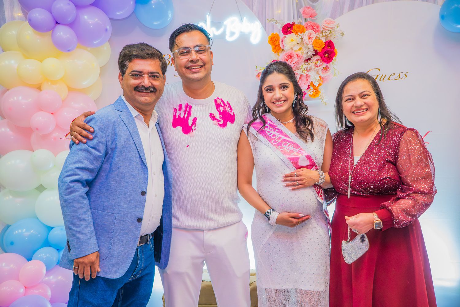 “Four friends standing together at a baby shower party, smiling in front of colorful decorations.”
