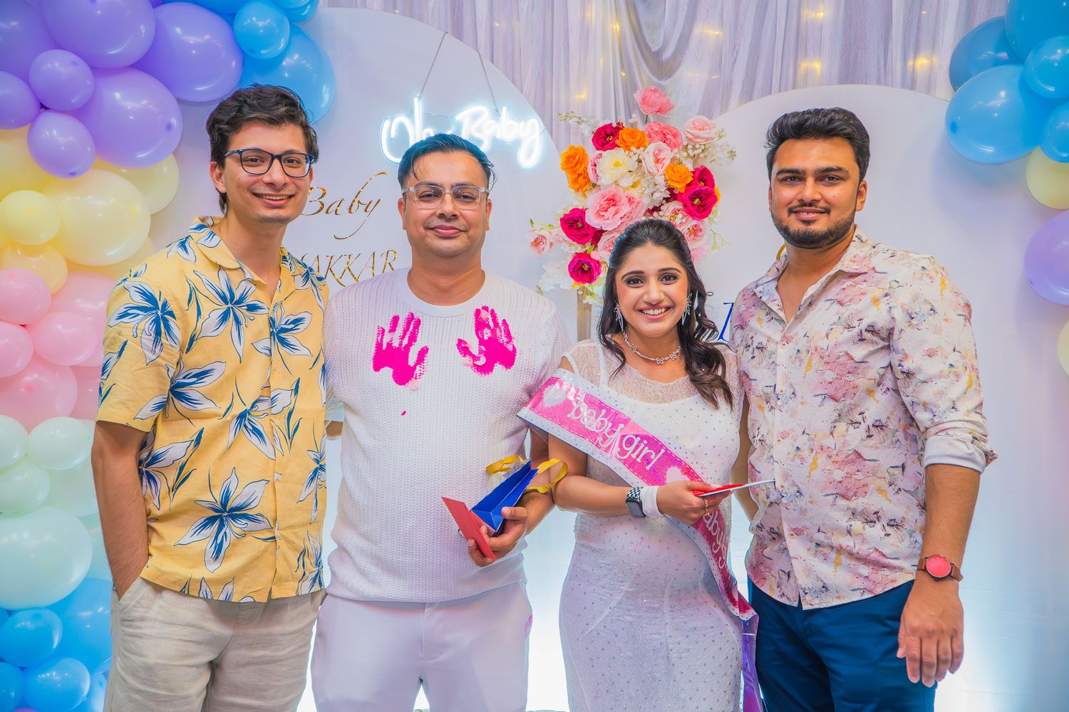 “Four friends standing together at a baby shower party, smiling in front of colorful decorations.”