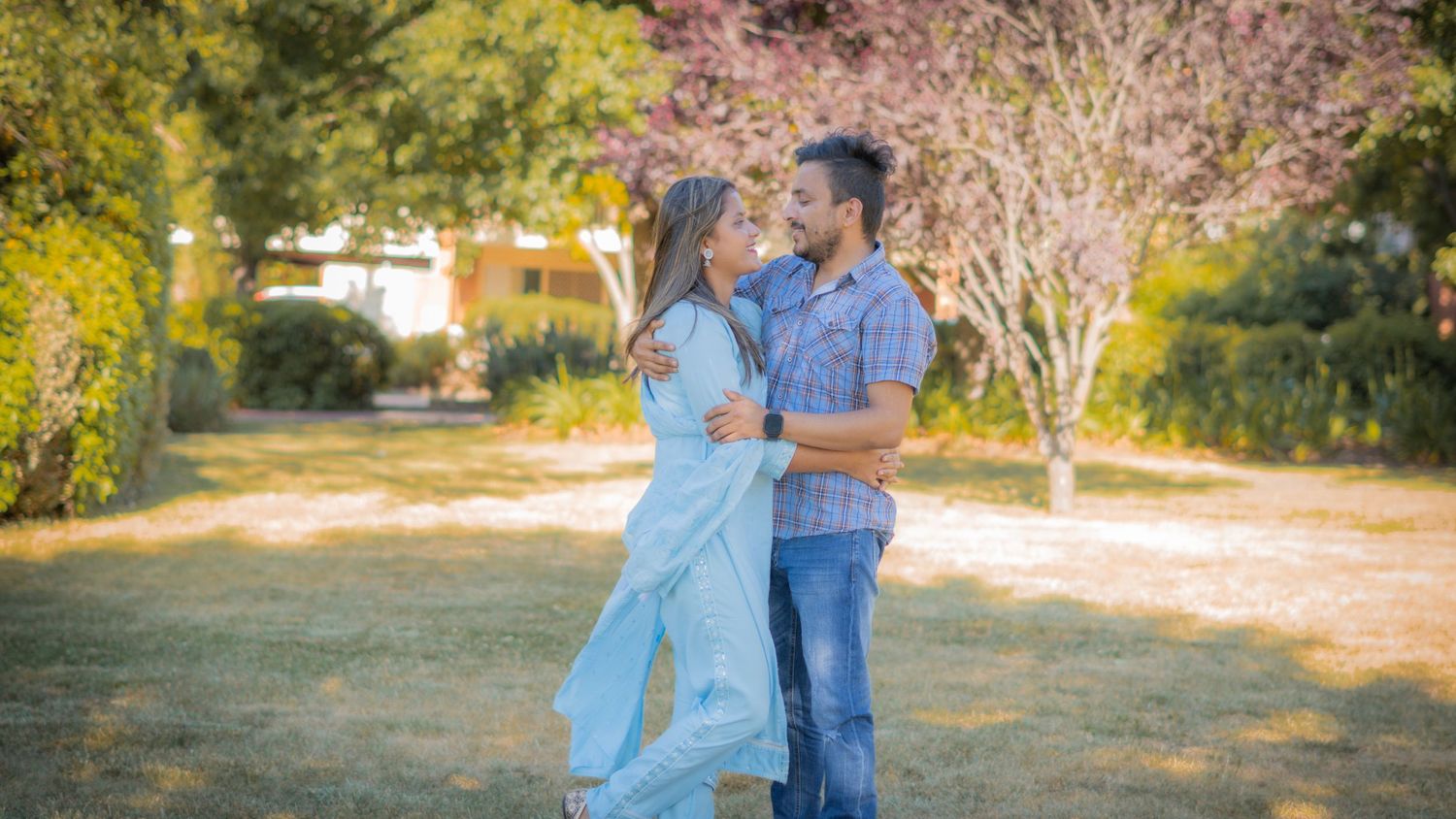 “Couple standing together in a sunny park, posing for a romantic outdoor photoshoot.”