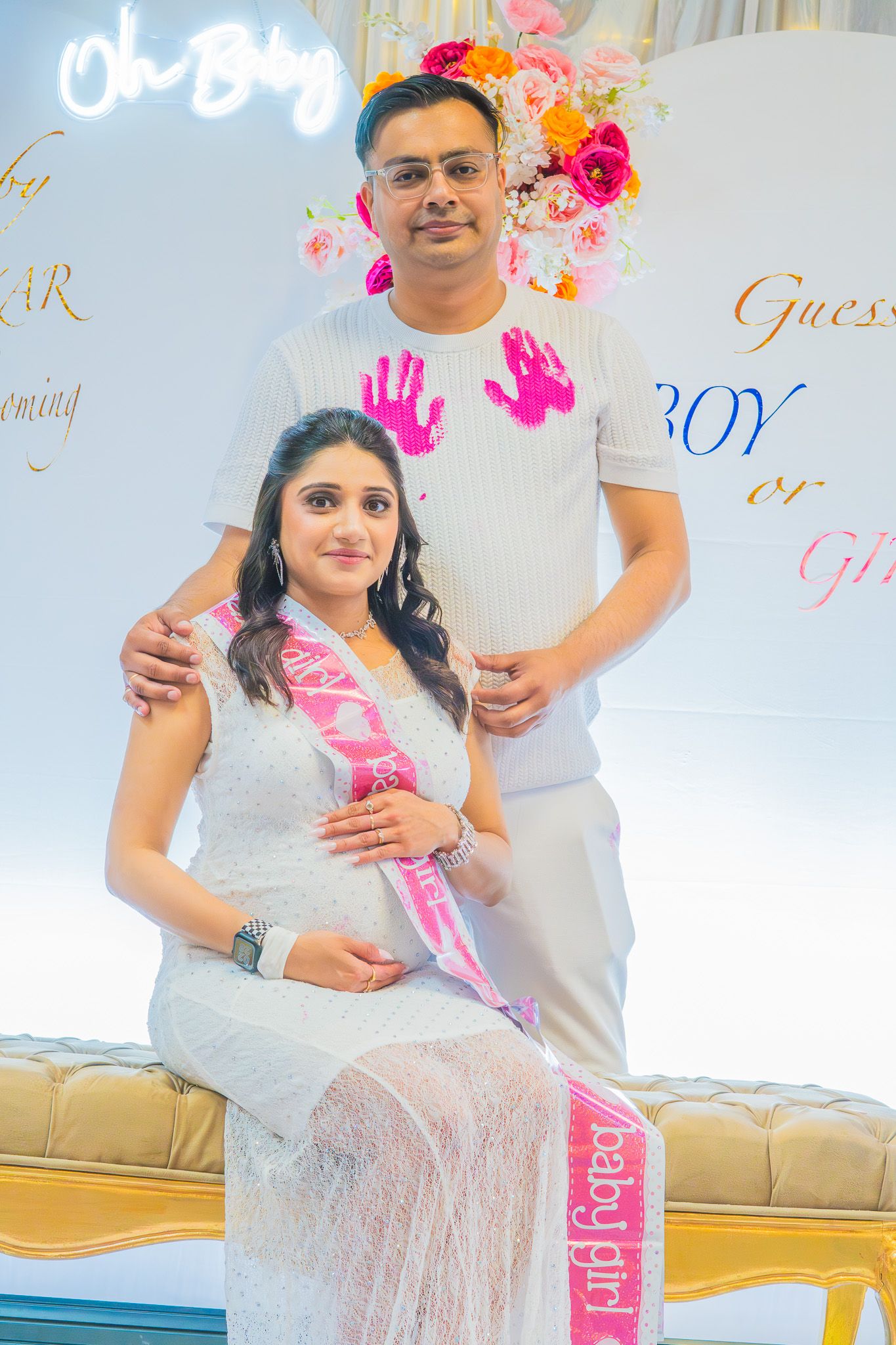 “Pregnant woman sitting on a decorated chair at a baby shower, smiling and holding her belly.”