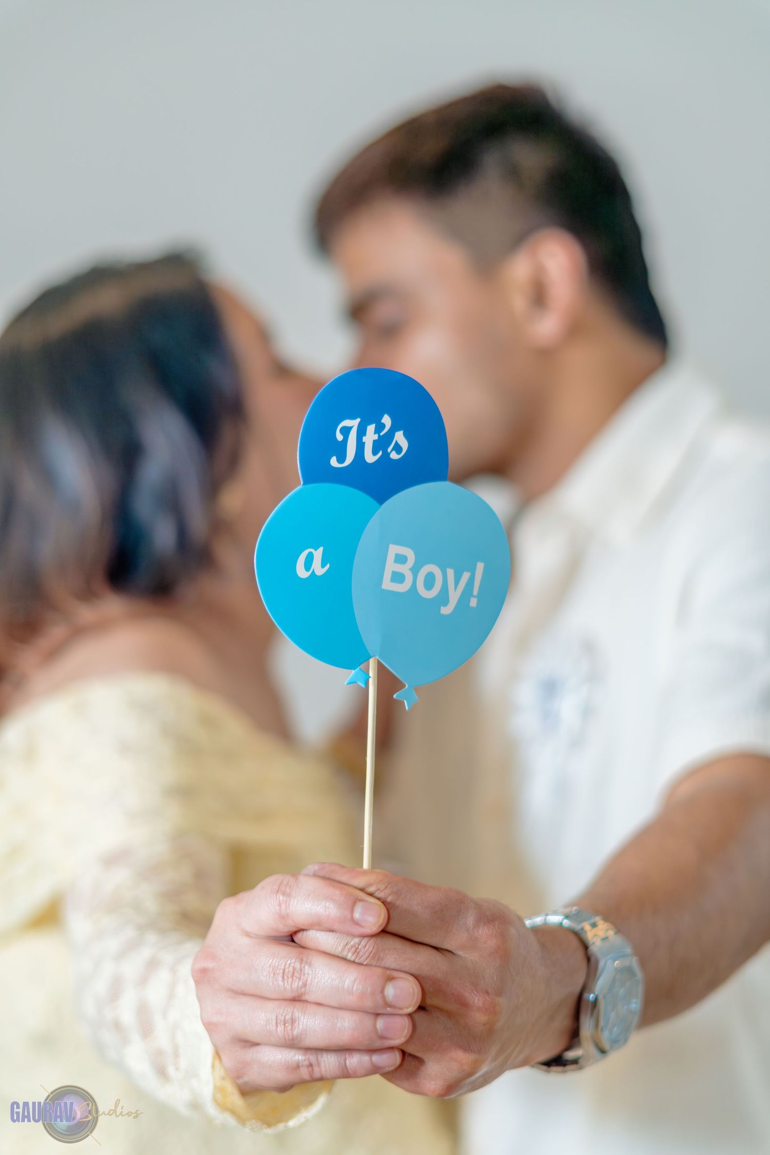 “Close-up of hands holding a small baby shower prop shaped like a blue rattle.”
