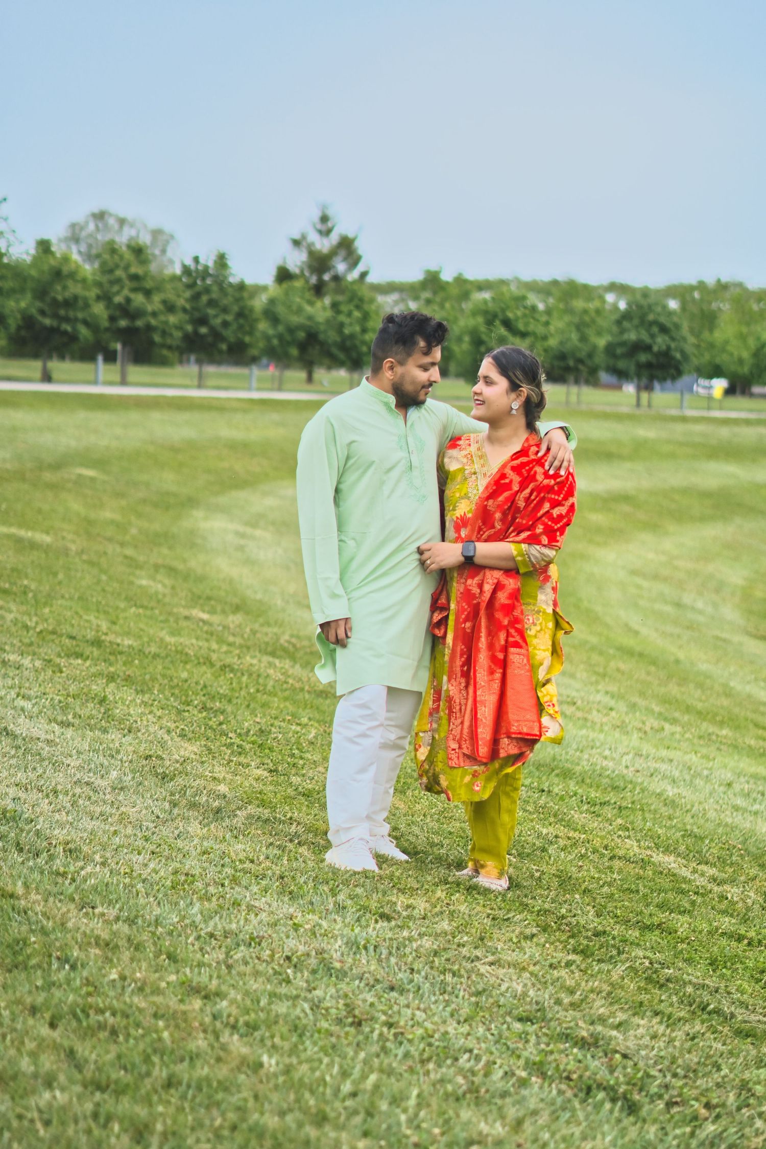 “Three people dressed in traditional outfits standing together in an open grassy field.”