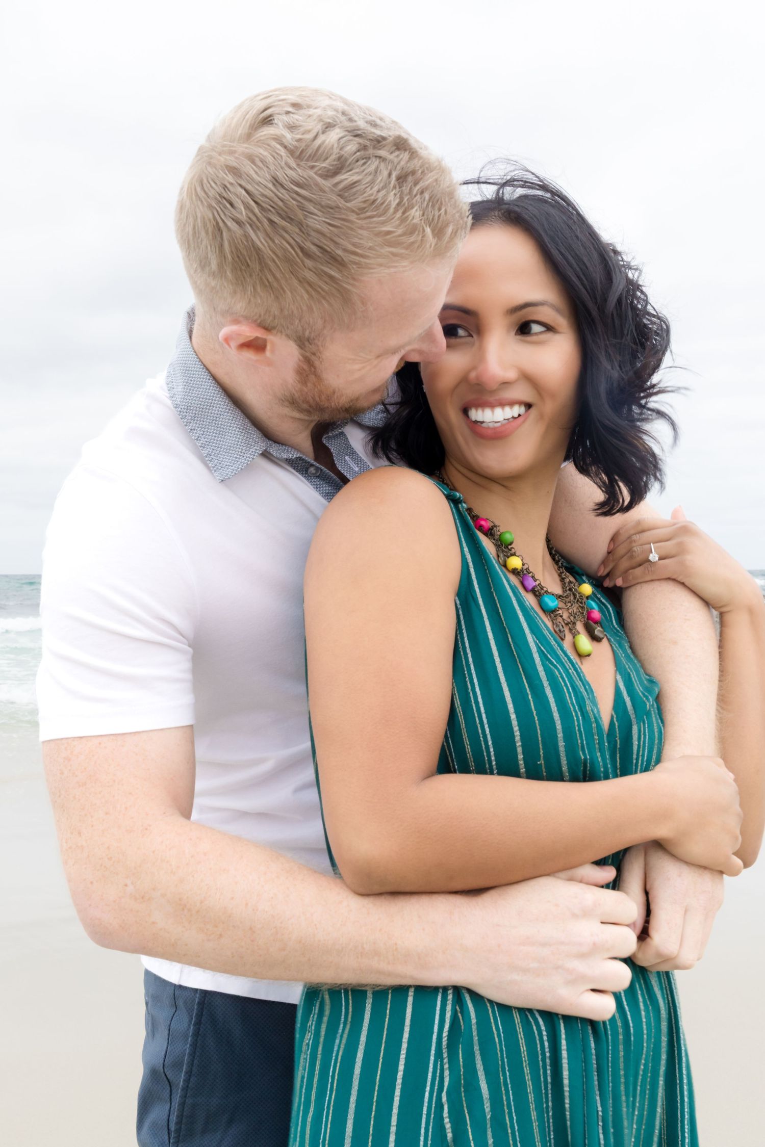 Romantic couple embracing on beach with woman in green striped dress.