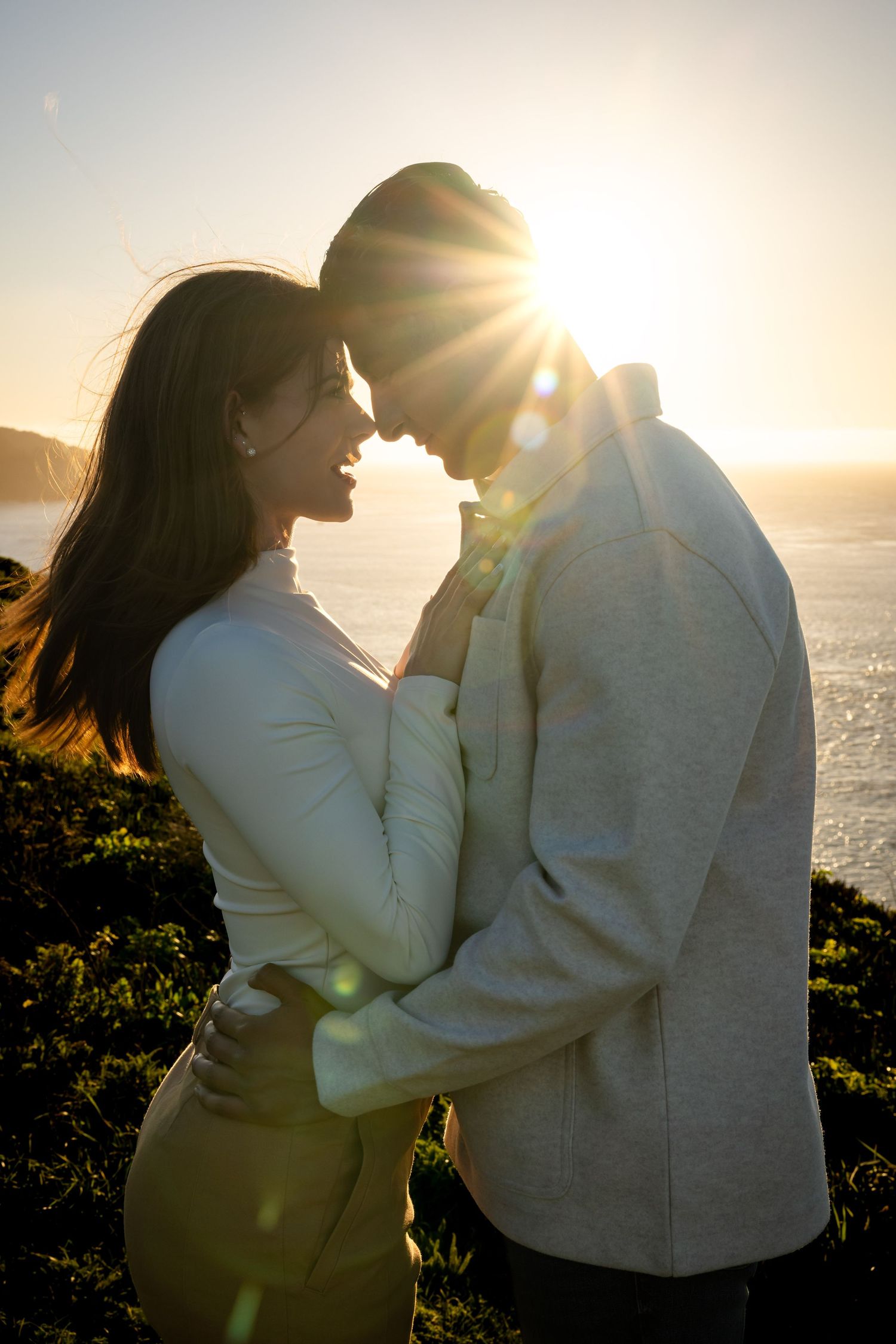 Silhouetted couple sharing intimate moment at sunset by ocean.