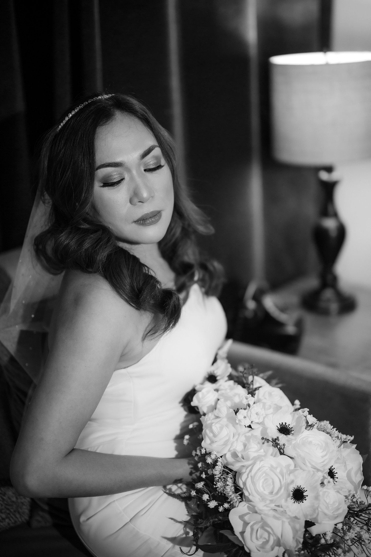 Black and white portrait of a bride holding a white rose bouquet in an elegant strapless wedding dress.