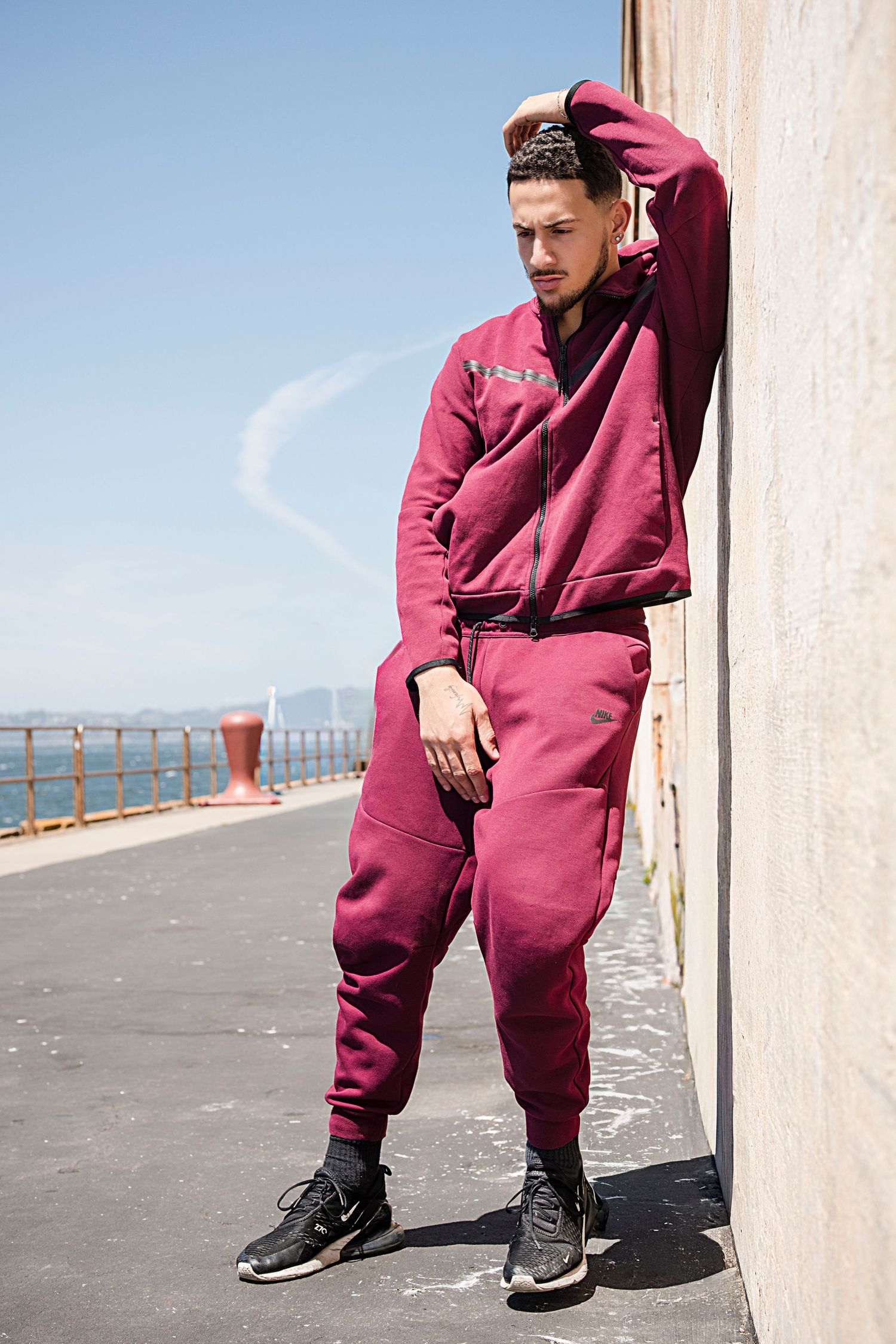 Athletic wear photoshoot featuring burgundy sweatsuit against coastal backdrop.