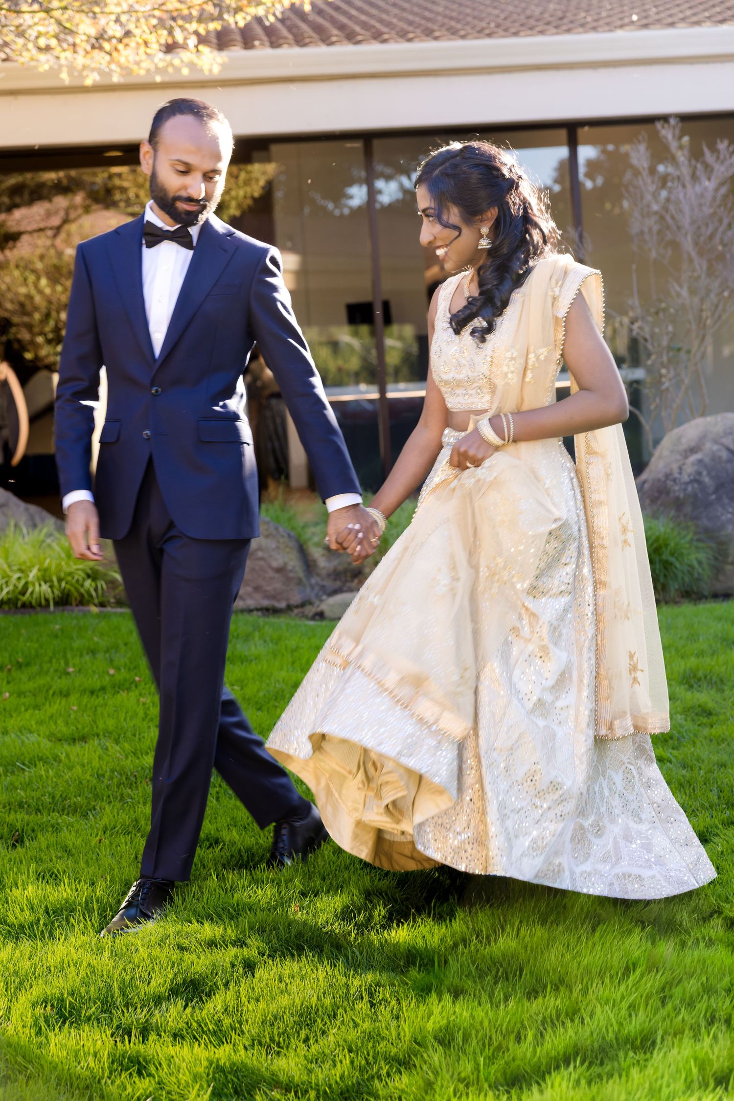 A couple dances on lush green grass in elegant wedding attire.