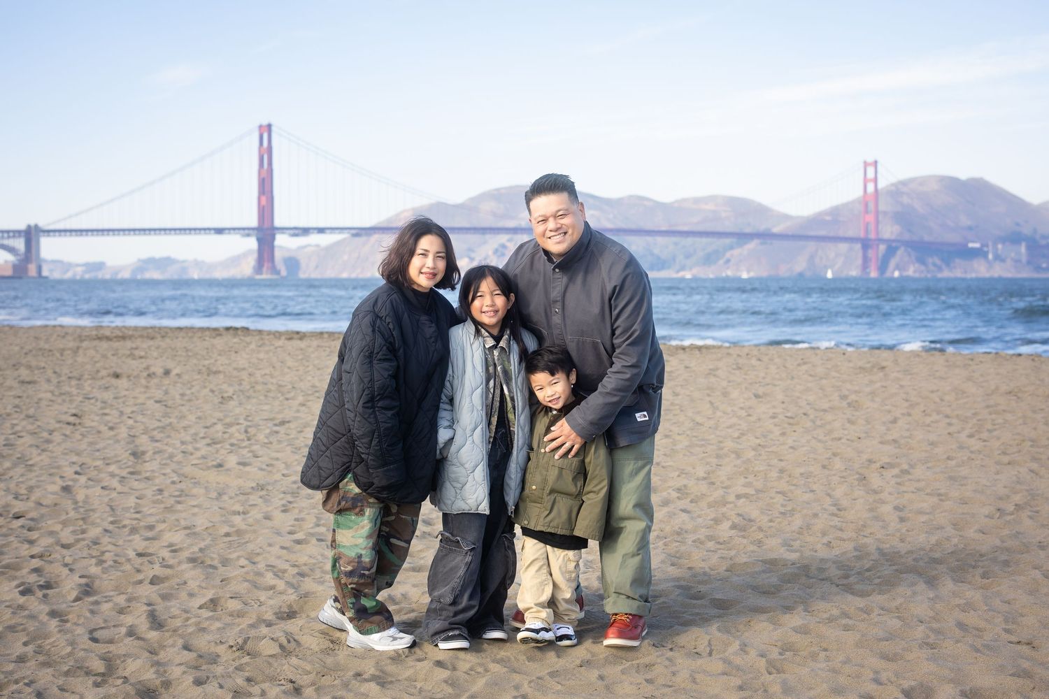 Group sitting together on sandy beach with Golden Gate Bridge visible in background.