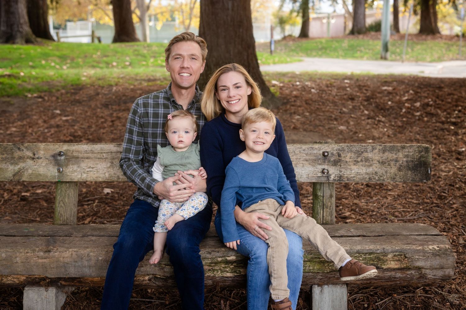 Casual family portrait session in park with autumn trees and natural lighting.