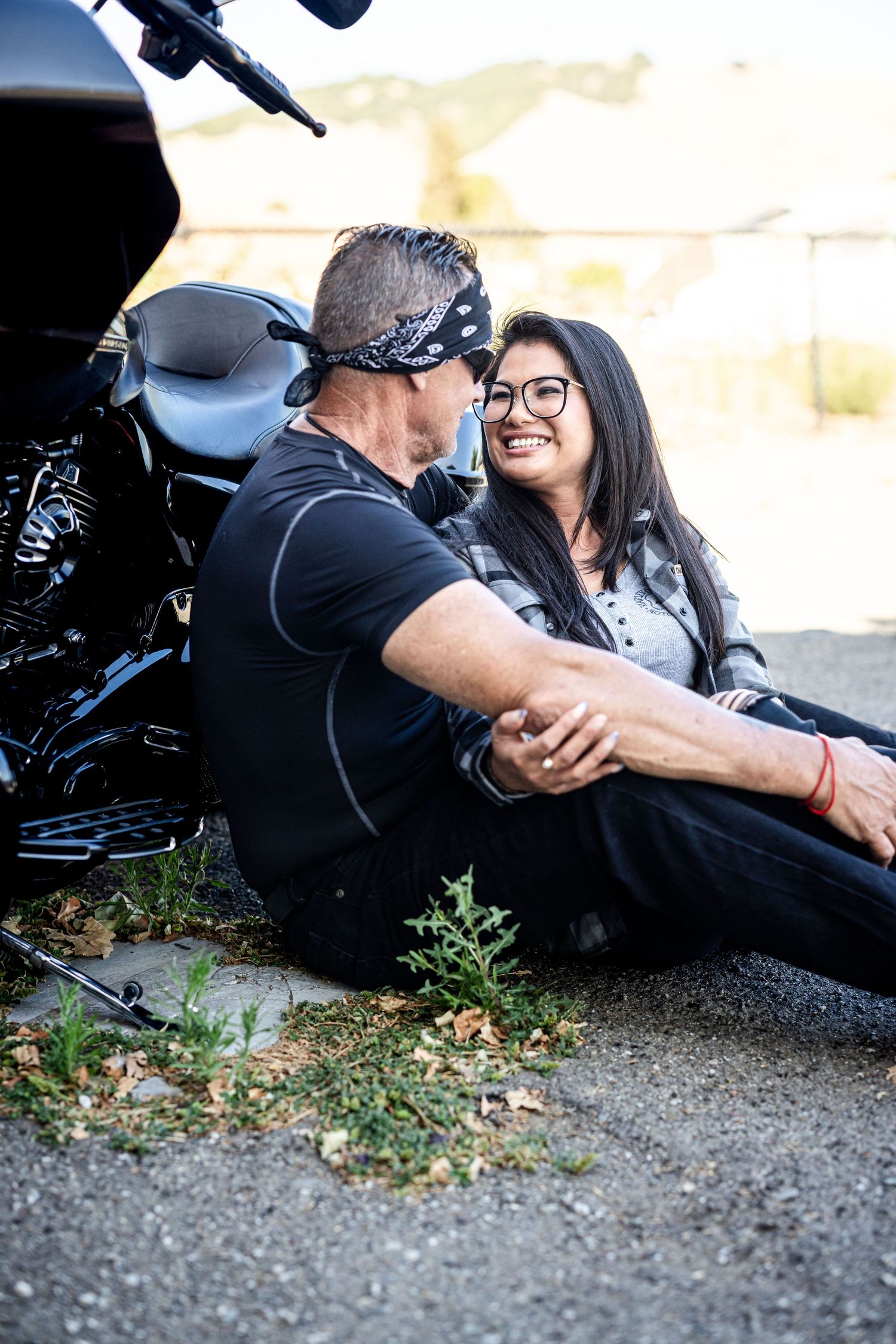A couple in casual attire lying on gravel ground in a playful sequence of candid engagement photos.