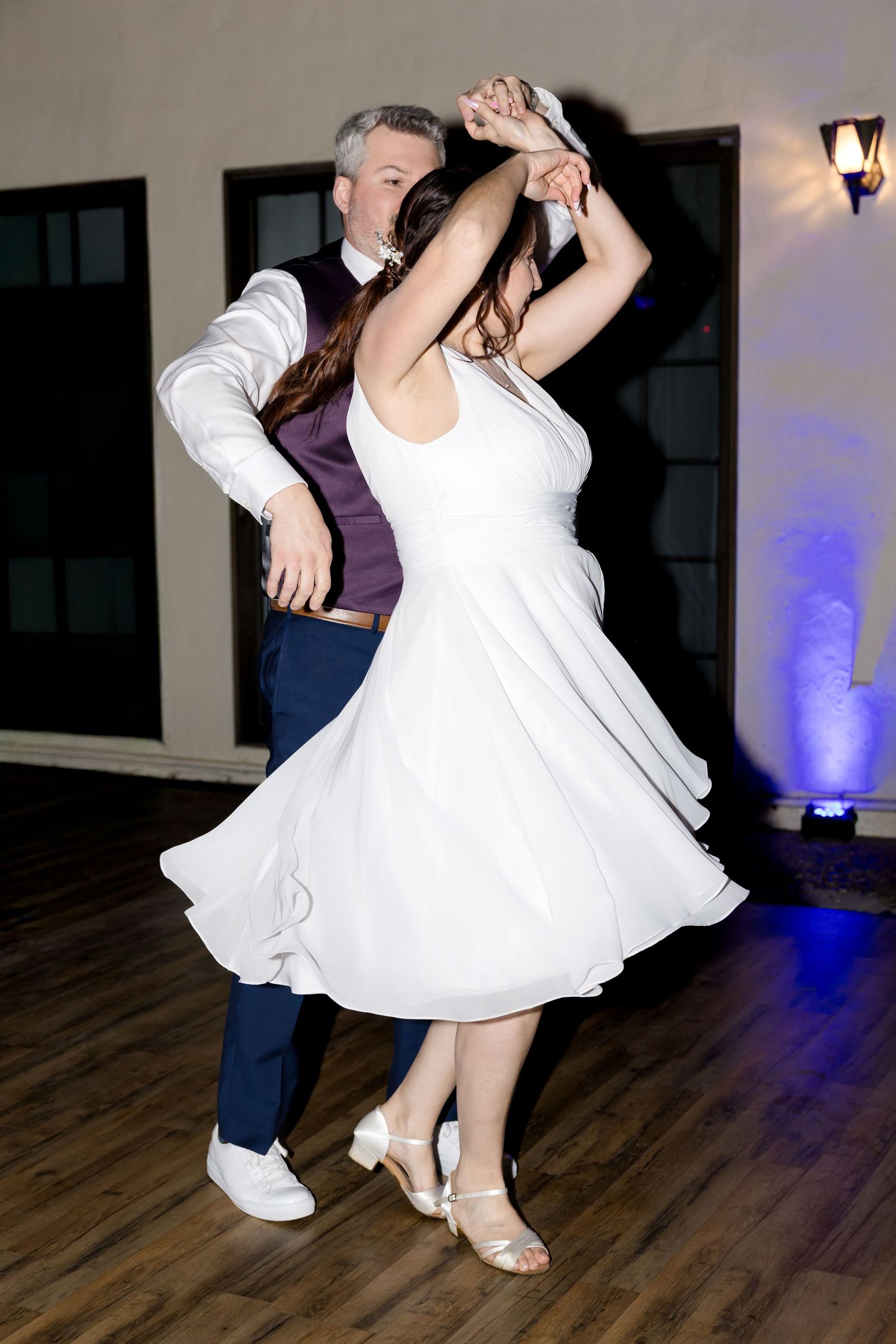 Couple dancing together on a wooden floor with twirling white dress and blue uplighting.