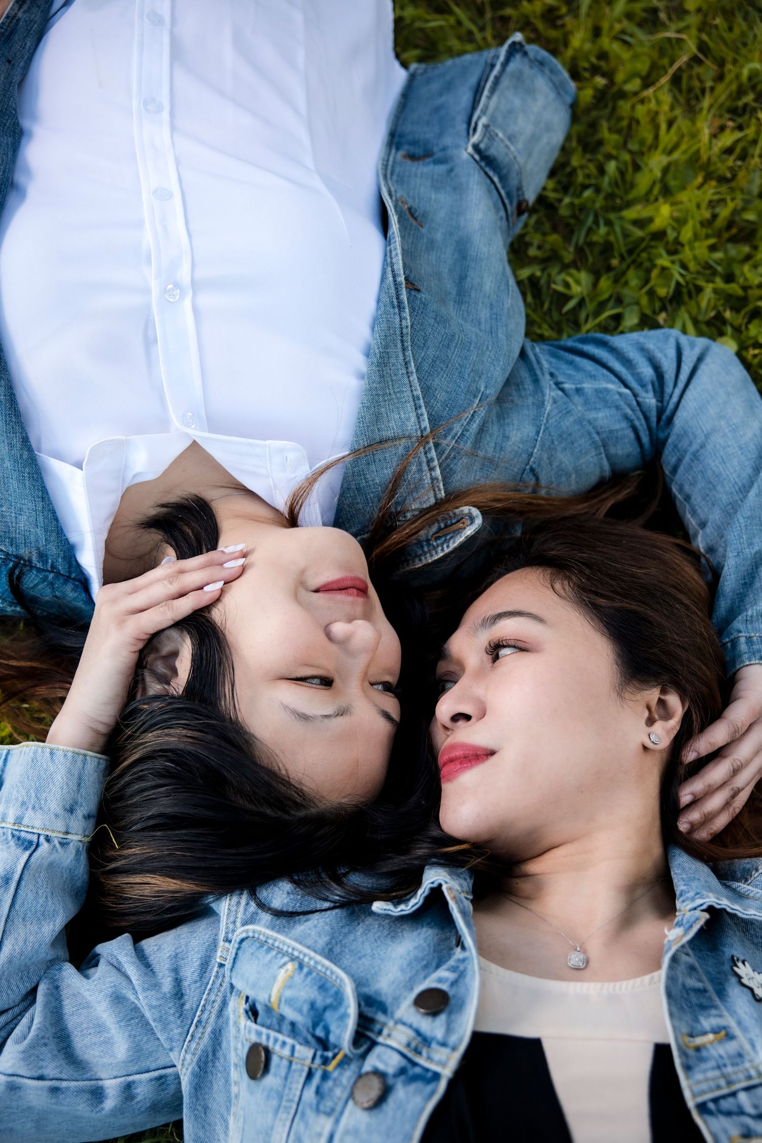 Couple lying head to head on grass wearing denim and white.