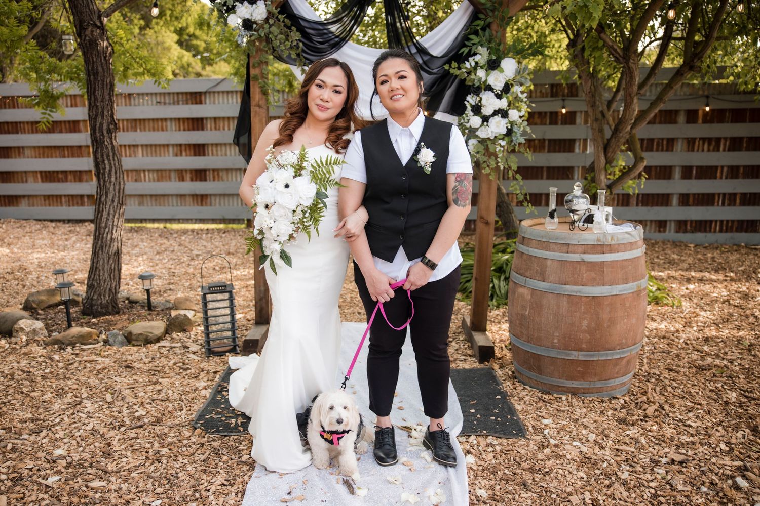 Wedding party poses in front of rustic wine barrels at an outdoor venue.