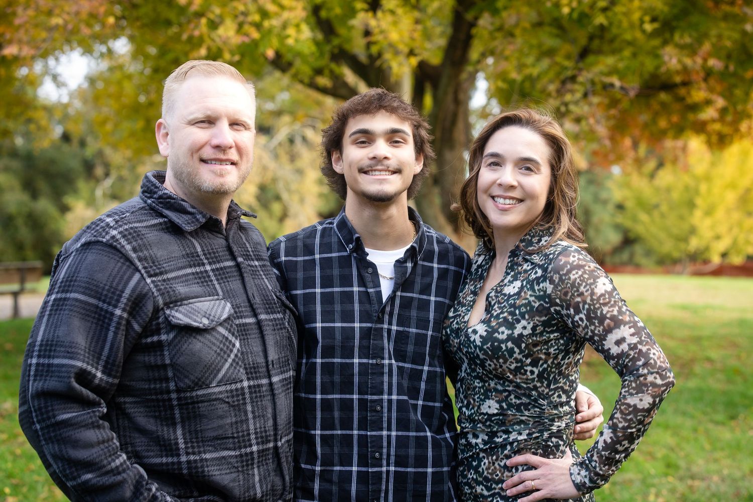 Casual outdoor family photo with fall colors and trees in the background.