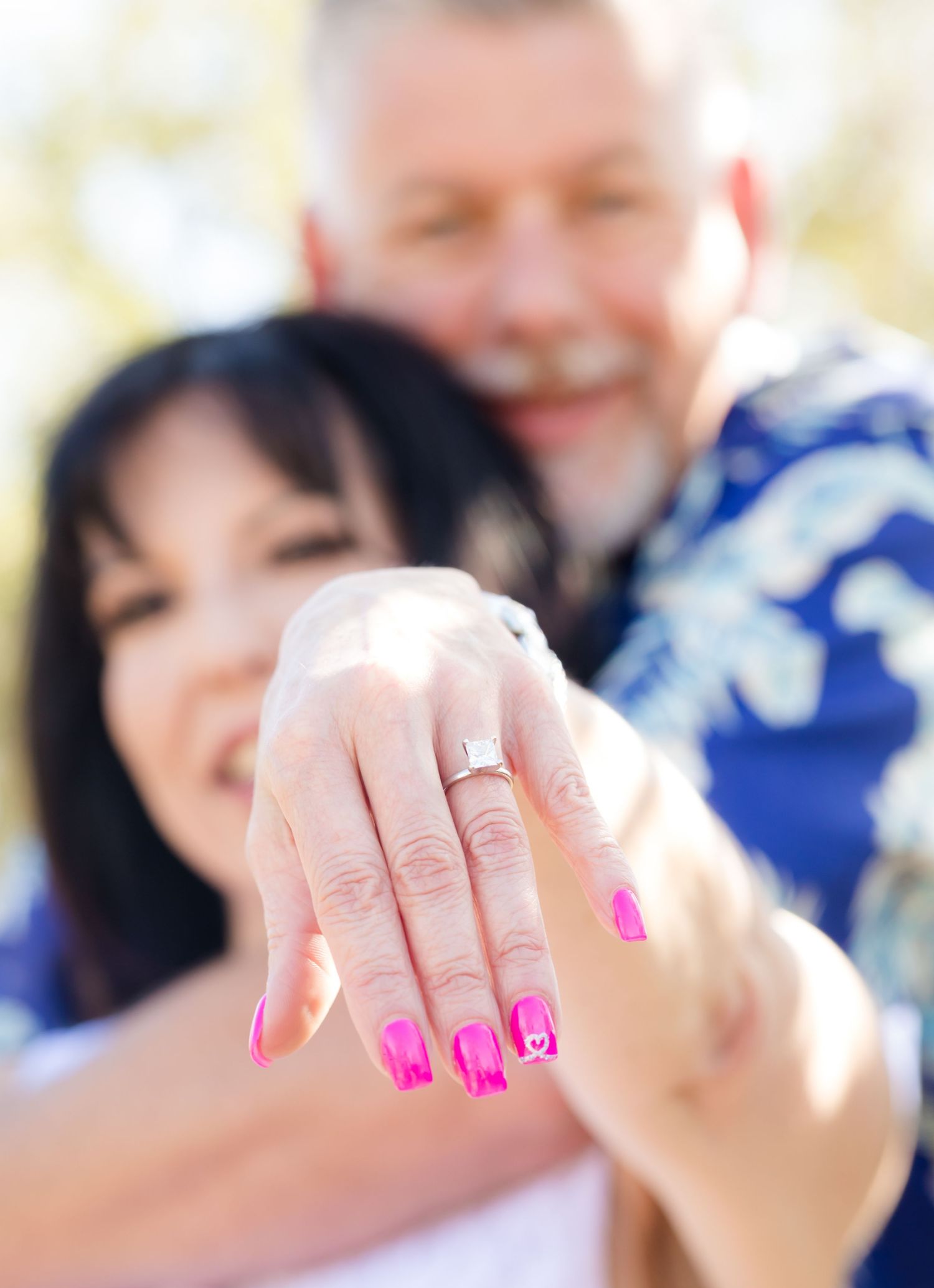 Close-up of engagement ring on hand with bright pink nail polish.