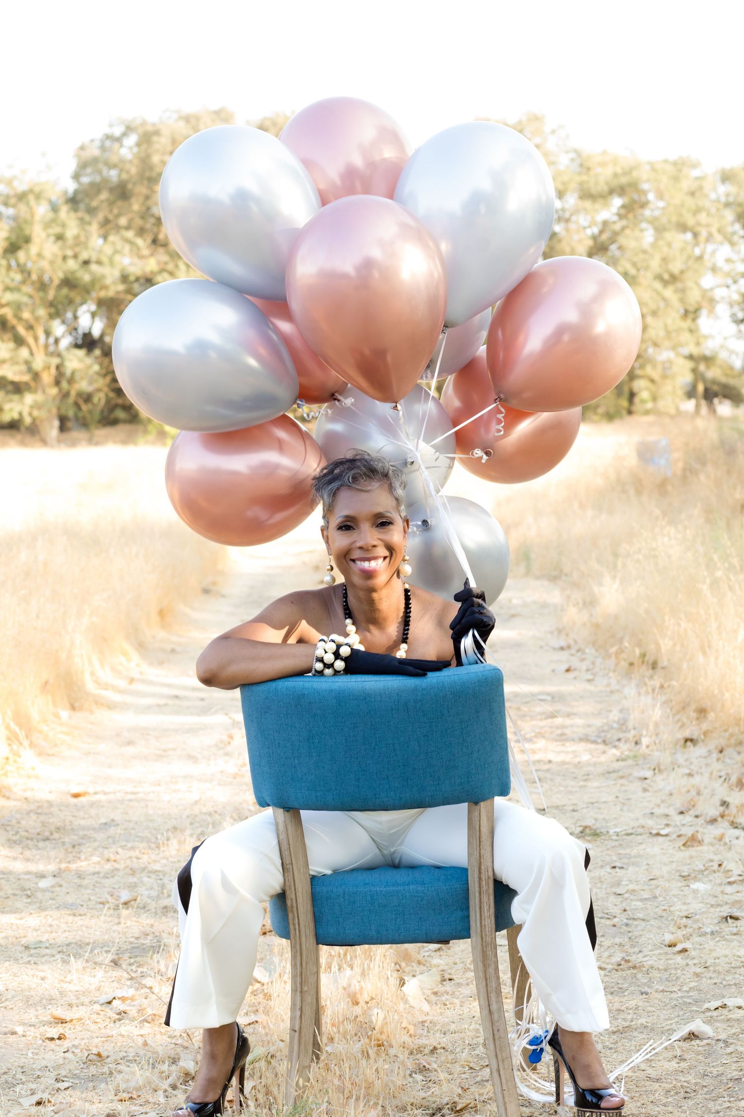 Blue chair with pink and white balloons in outdoor setting during golden hour.
