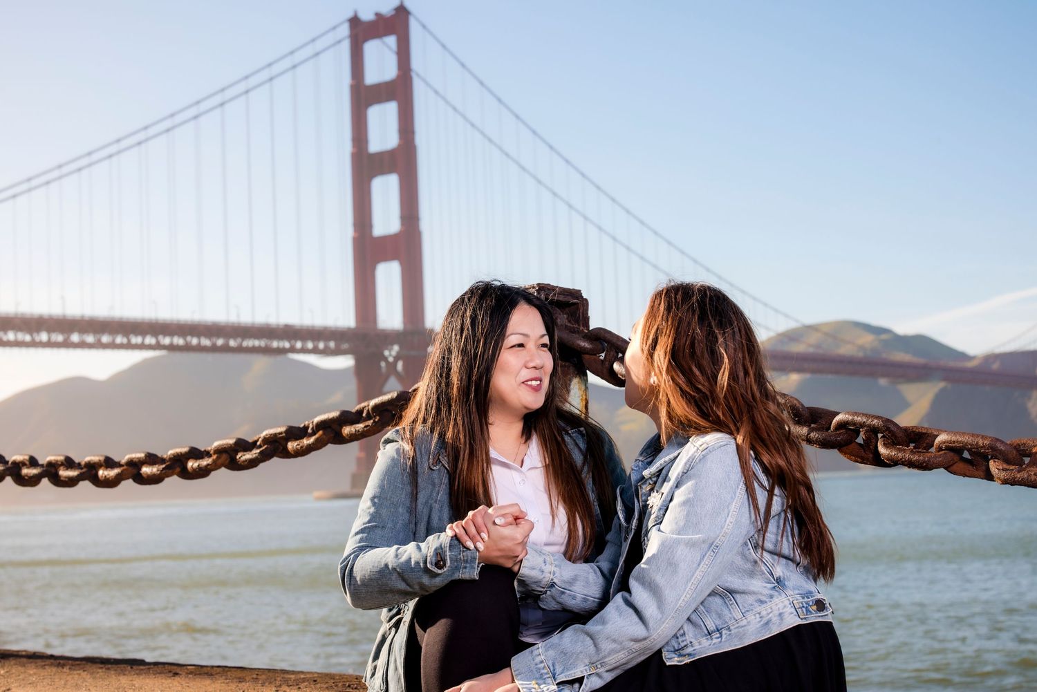 Couple poses playfully with Golden Gate Bridge visible in background on sunny day.
