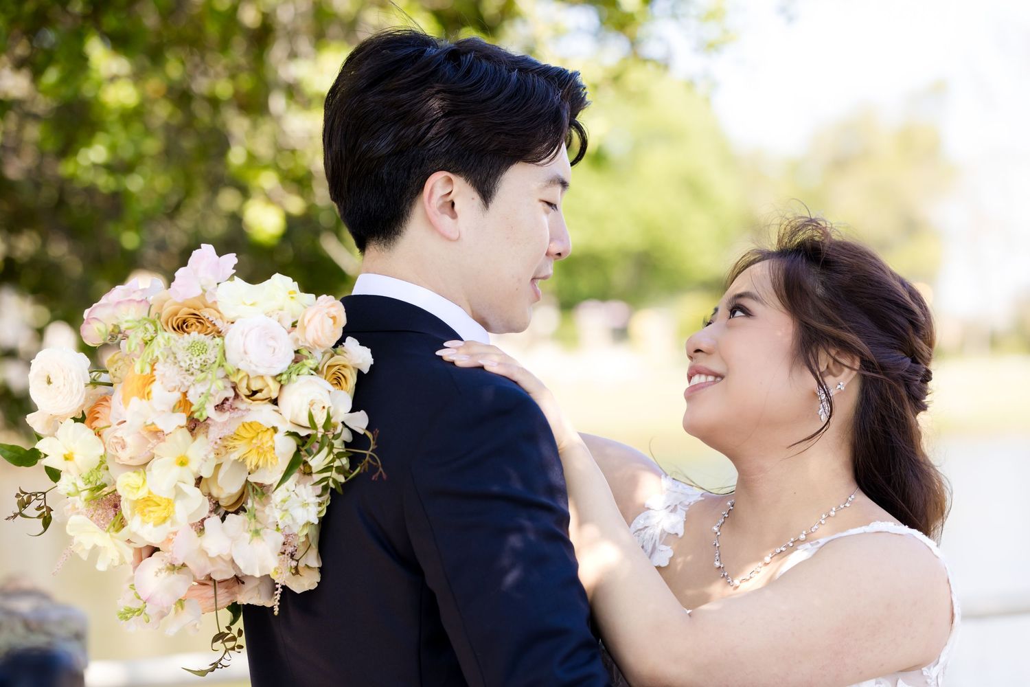 Romantic wedding couple sharing a joyful moment with a beautiful peach and cream floral bouquet.
