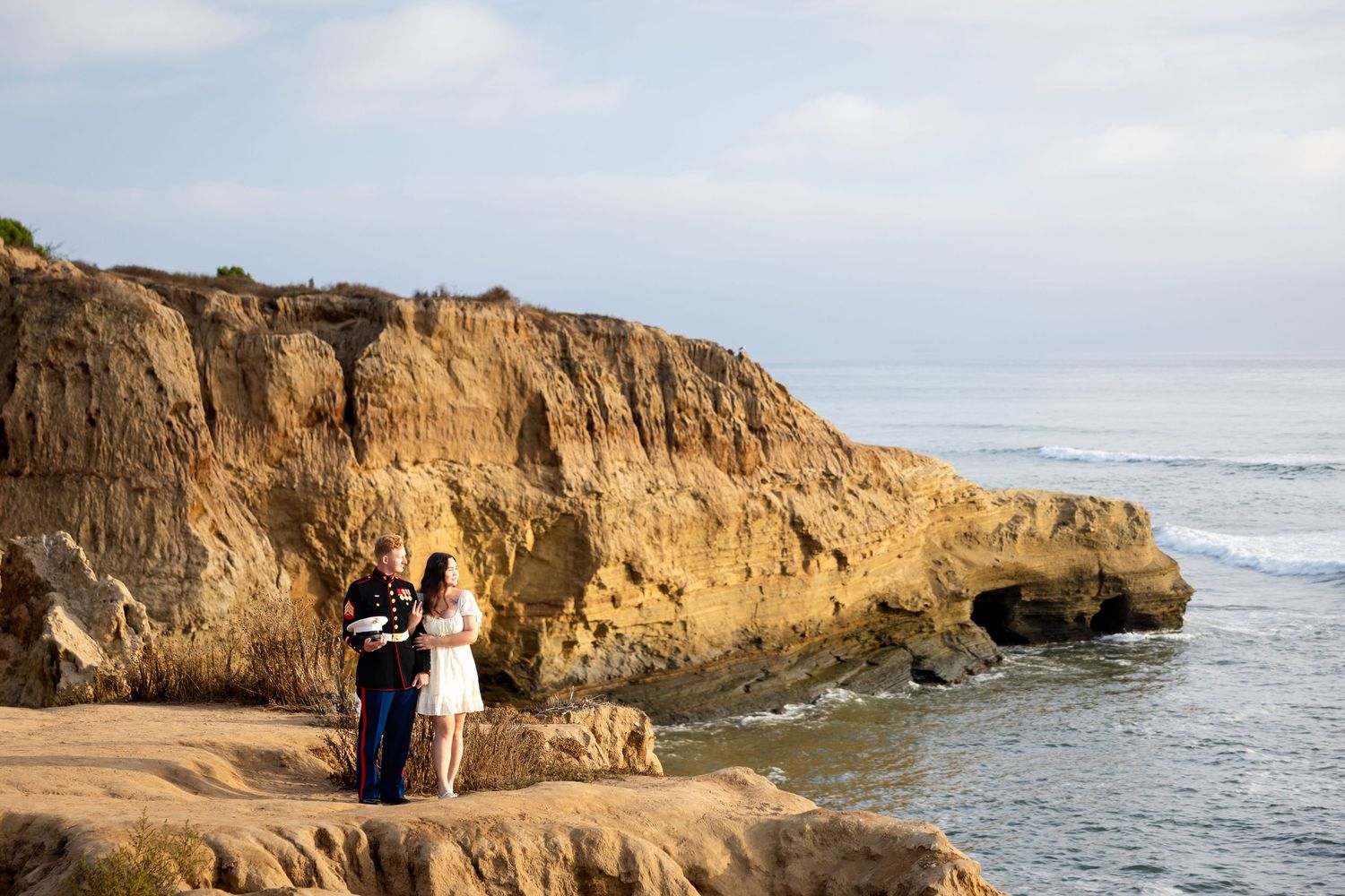 Couple and officiant exchange vows on rocky coastal cliffs overlooking the ocean at sunset.