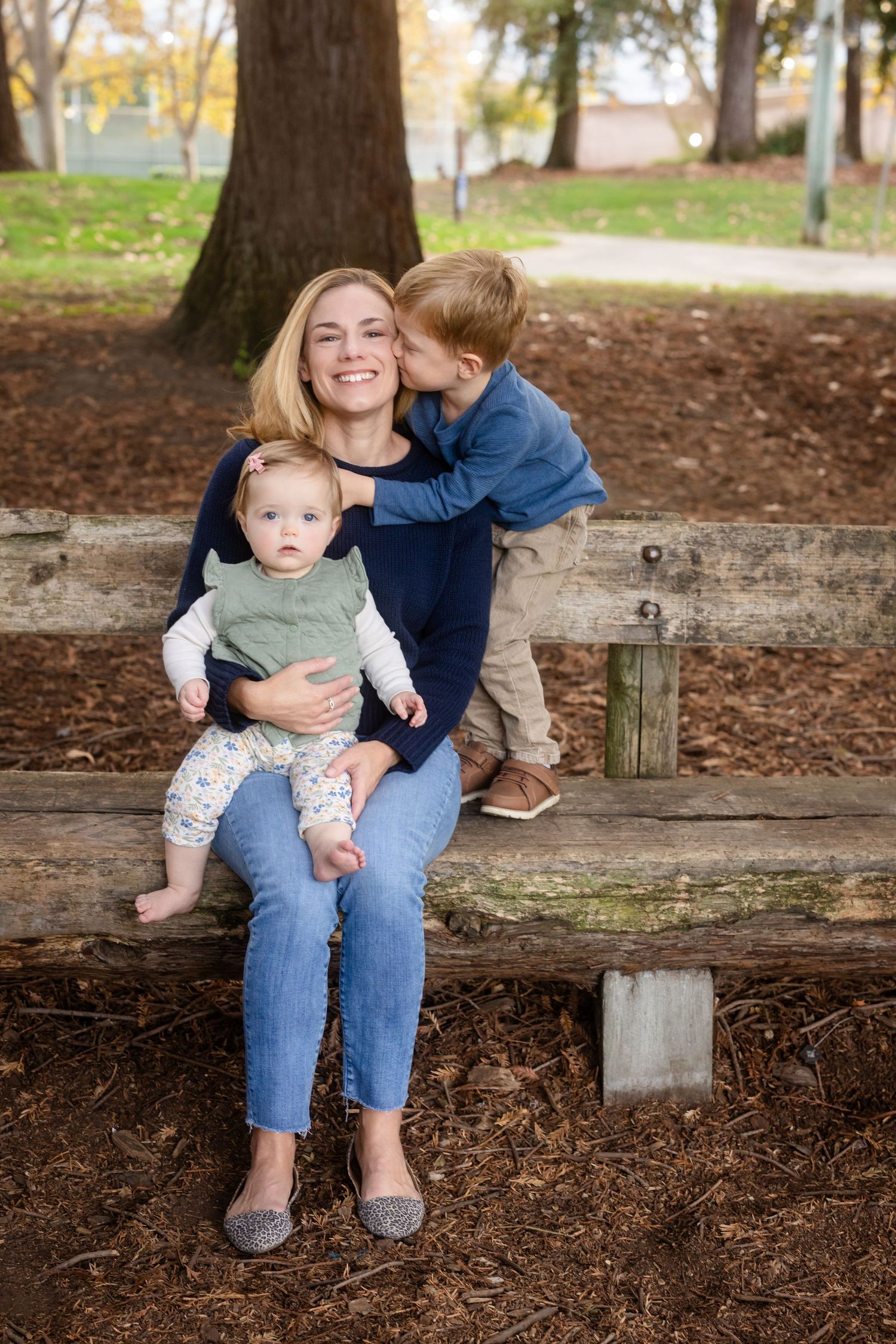 People sharing tender moments while sitting on a wooden bench in a park.