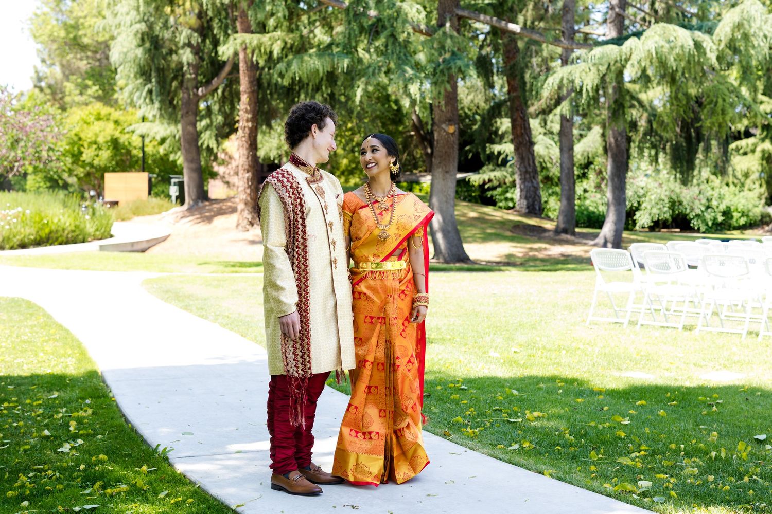 Wedding party members walk along a sunlit garden path in colorful traditional attire.