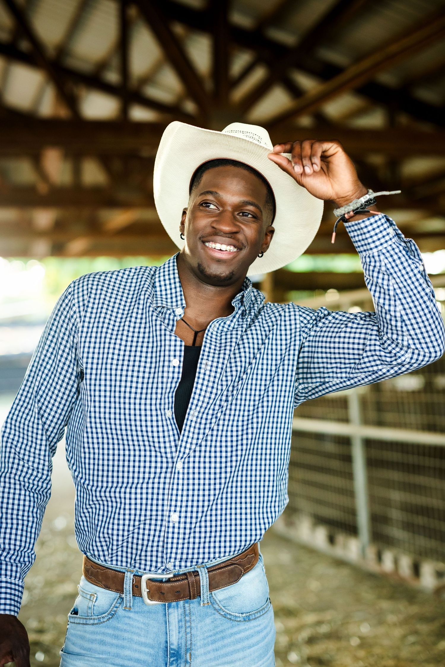 Person in western attire and cowboy hat posing in front of barn setting.