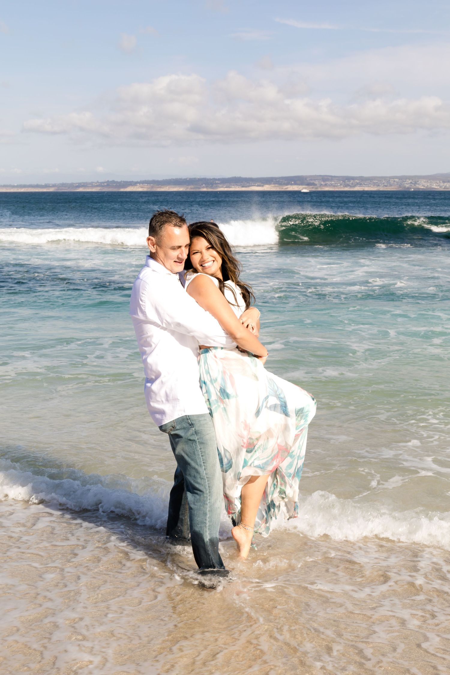 Happy couple embracing on a beach with crashing waves in the background.