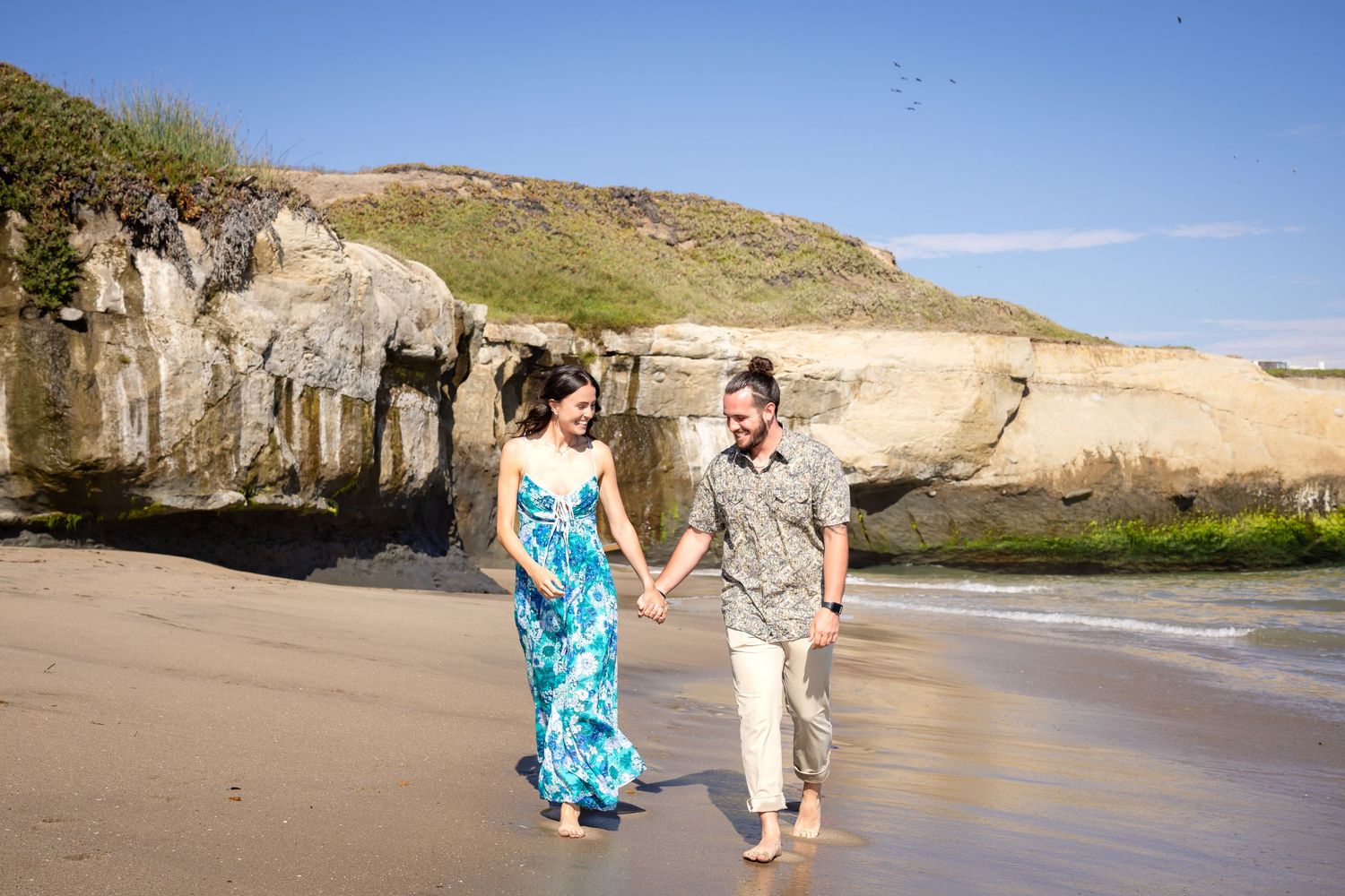 Couple walking and dancing along scenic coastal beach with cliffs.