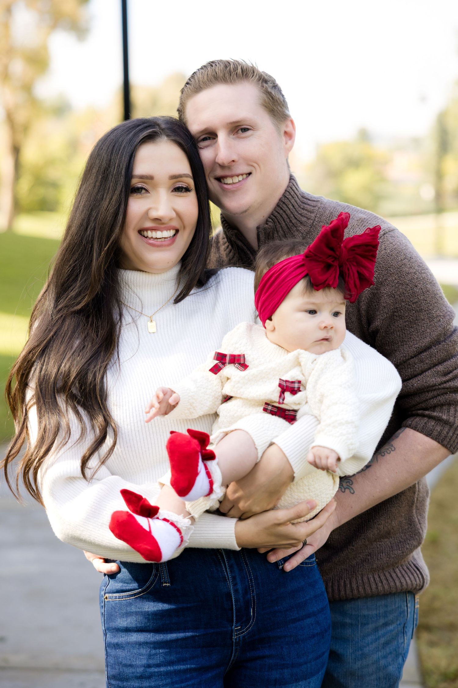 Family in coordinating white and brown sweaters pose for holiday portrait outdoors.