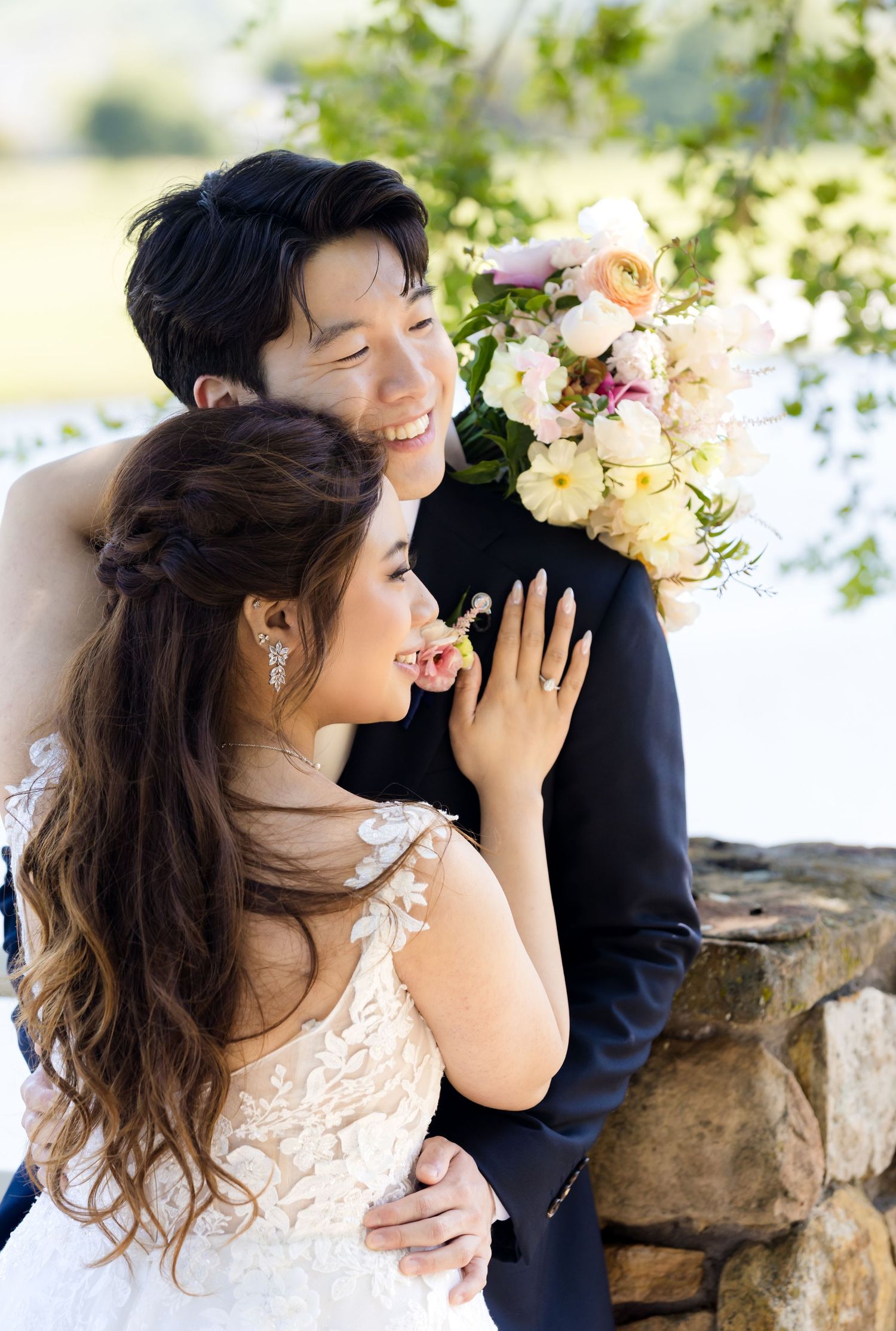 Romantic wedding couple shares joyful moments together against stone wall backdrop with blooming flowers.