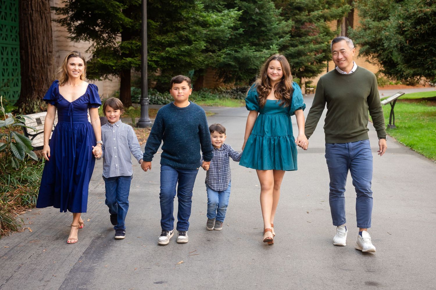 Family members walking together on a paved path through a park on an autumn day.