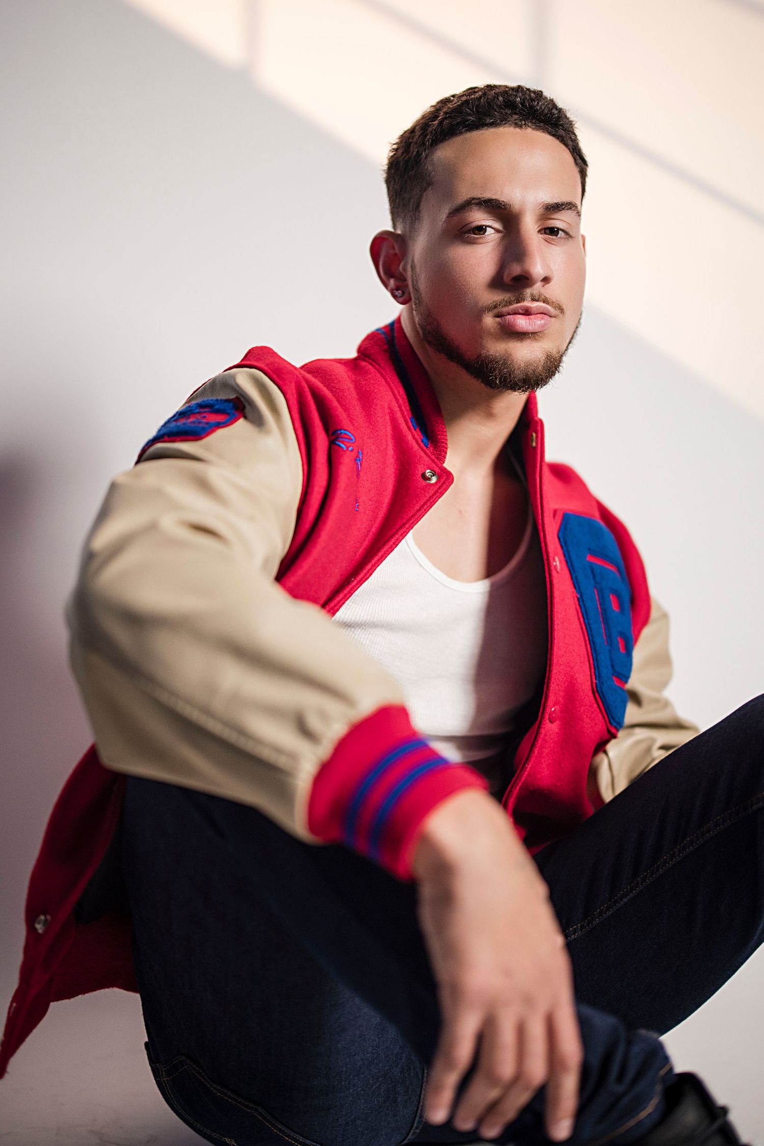 Fashion portrait series in red and beige varsity jacket against white studio background.