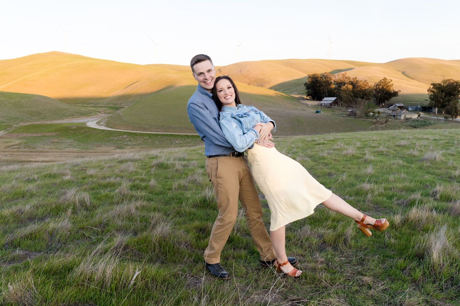 Couple posing playfully in grassy field during golden hour.