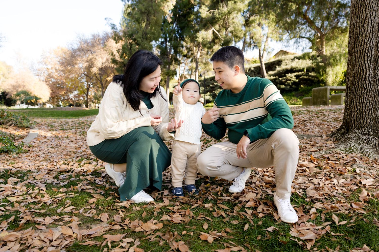 Family sitting together on fallen autumn leaves in a park setting.